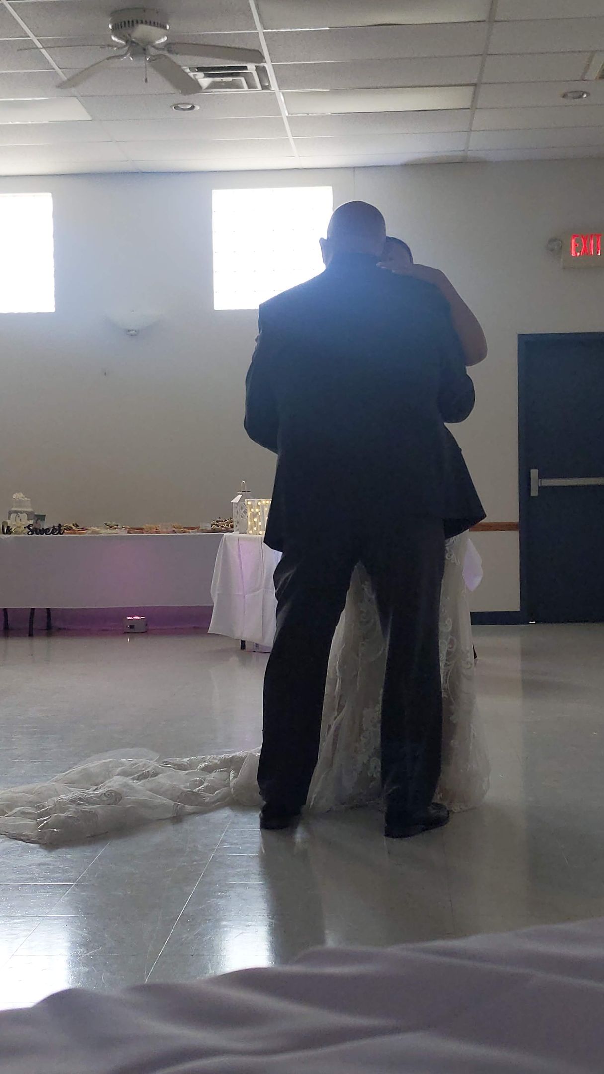Two people standing in a bright indoor room with a polished floor and windows.