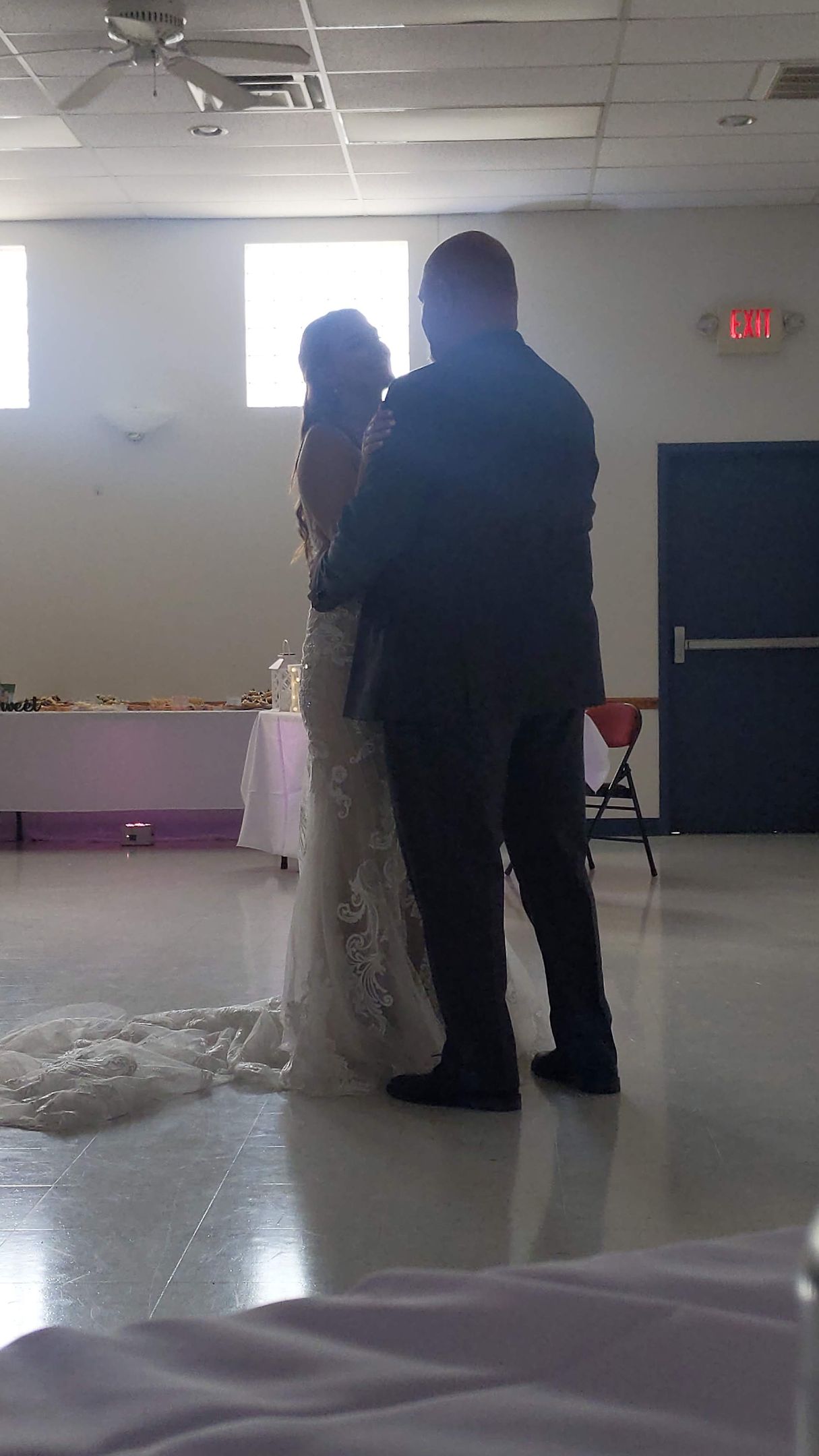Couple dancing at a wedding reception in a bright hall, bride in white gown and groom in dark suit