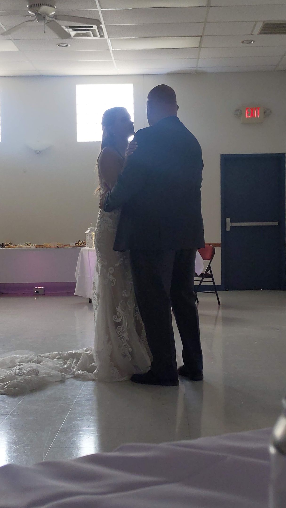 Couple slow dancing at an indoor event, woman in a white dress and man in a dark suit.