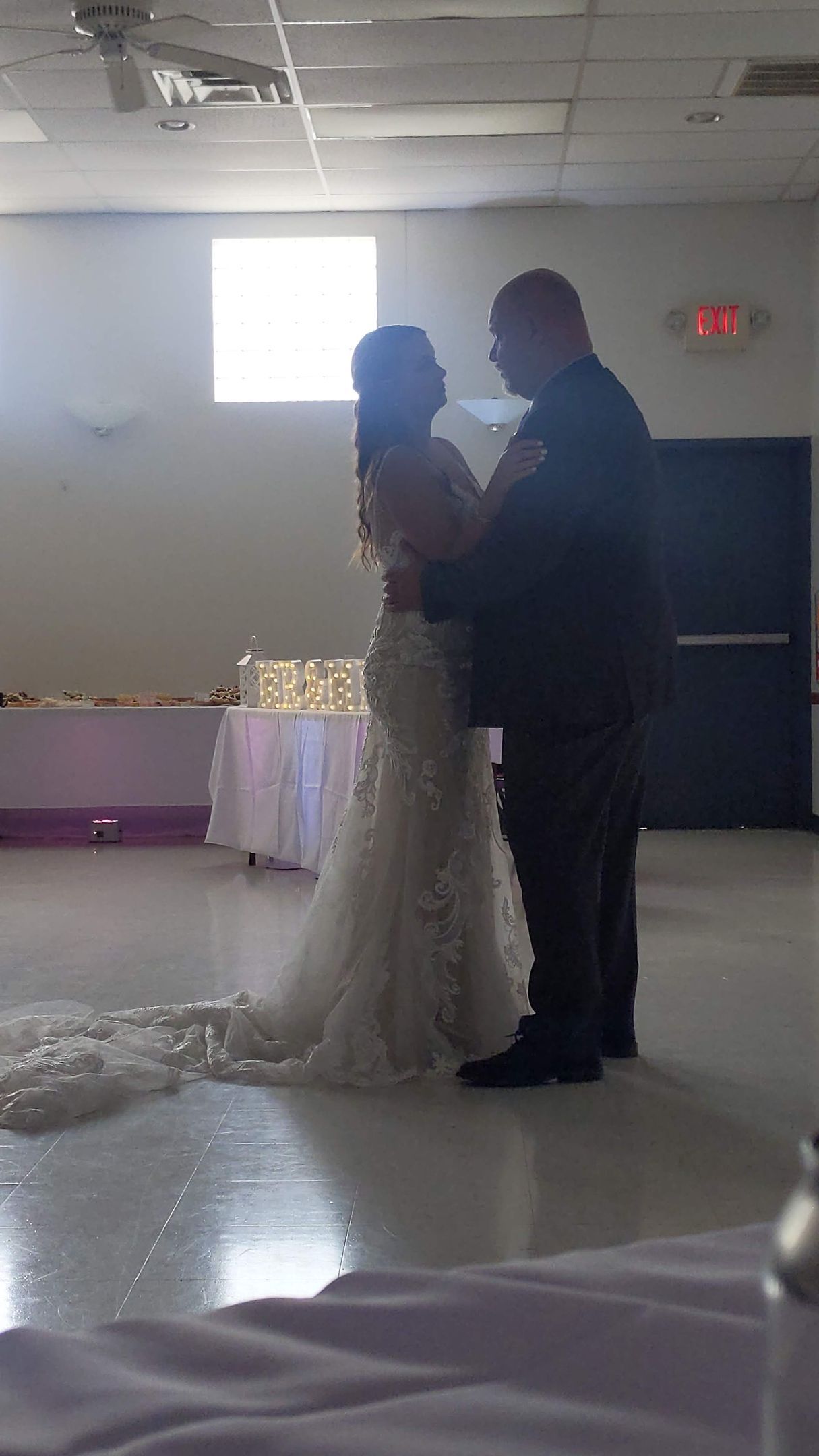 Bride and groom standing close together in a decorated indoor reception hall, facing each other at their wedding.