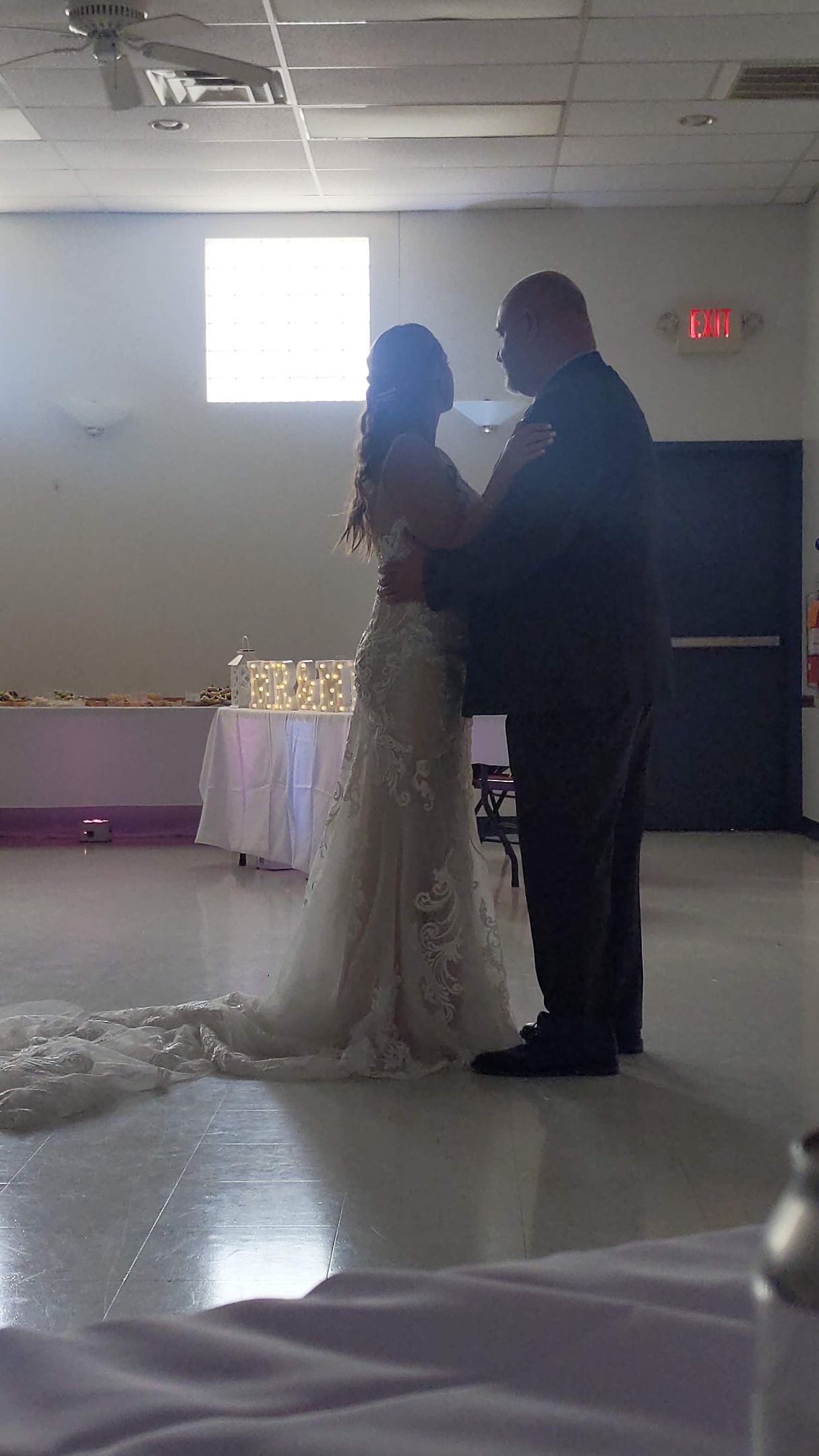 Bride and groom standing together at a dimly lit indoor wedding reception, facing each other.