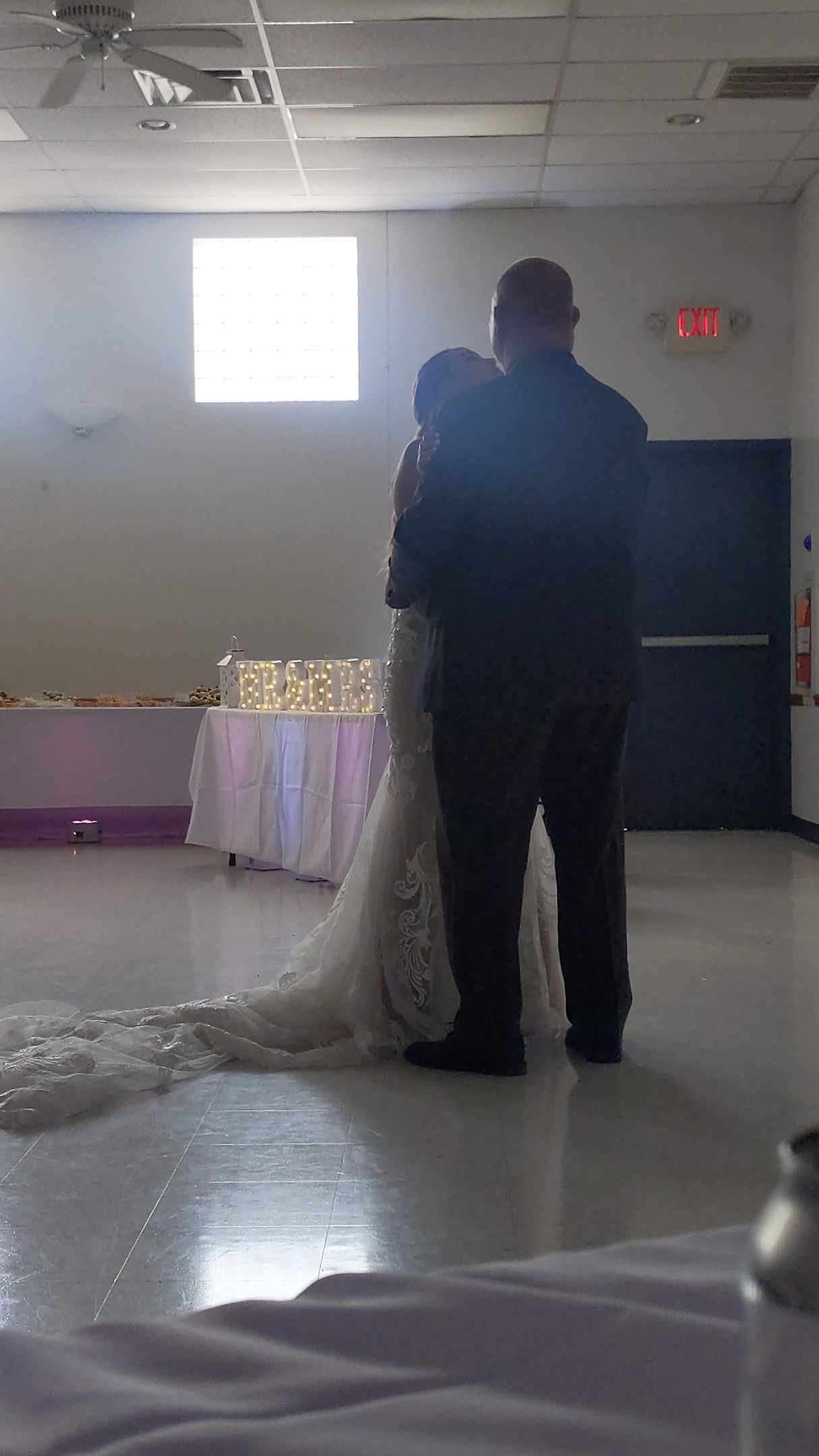 Couple dancing at a reception in a dim banquet hall, bride in a white gown and groom in dark attire