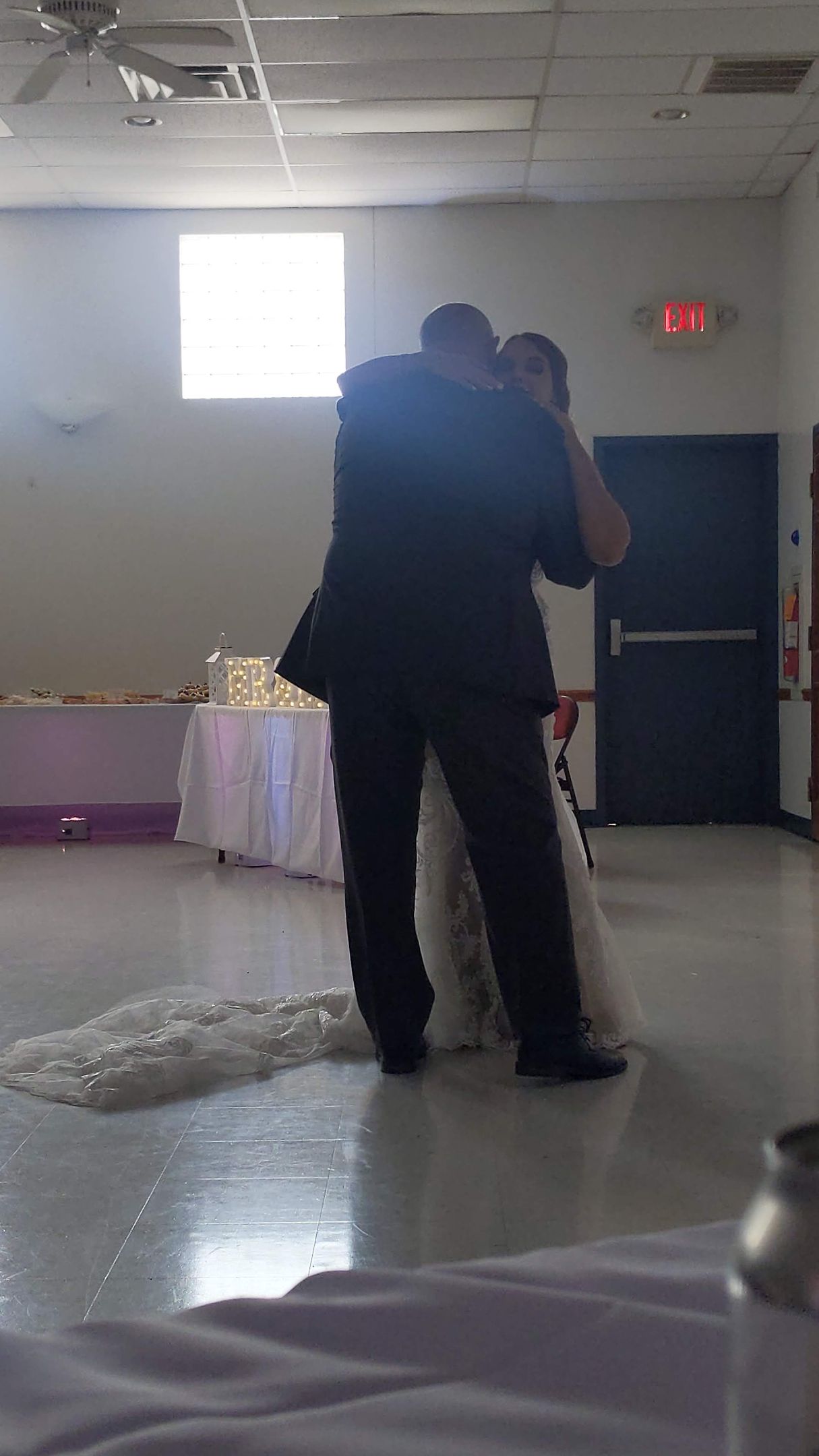Two people dancing closely in a banquet hall with white and purple decor.