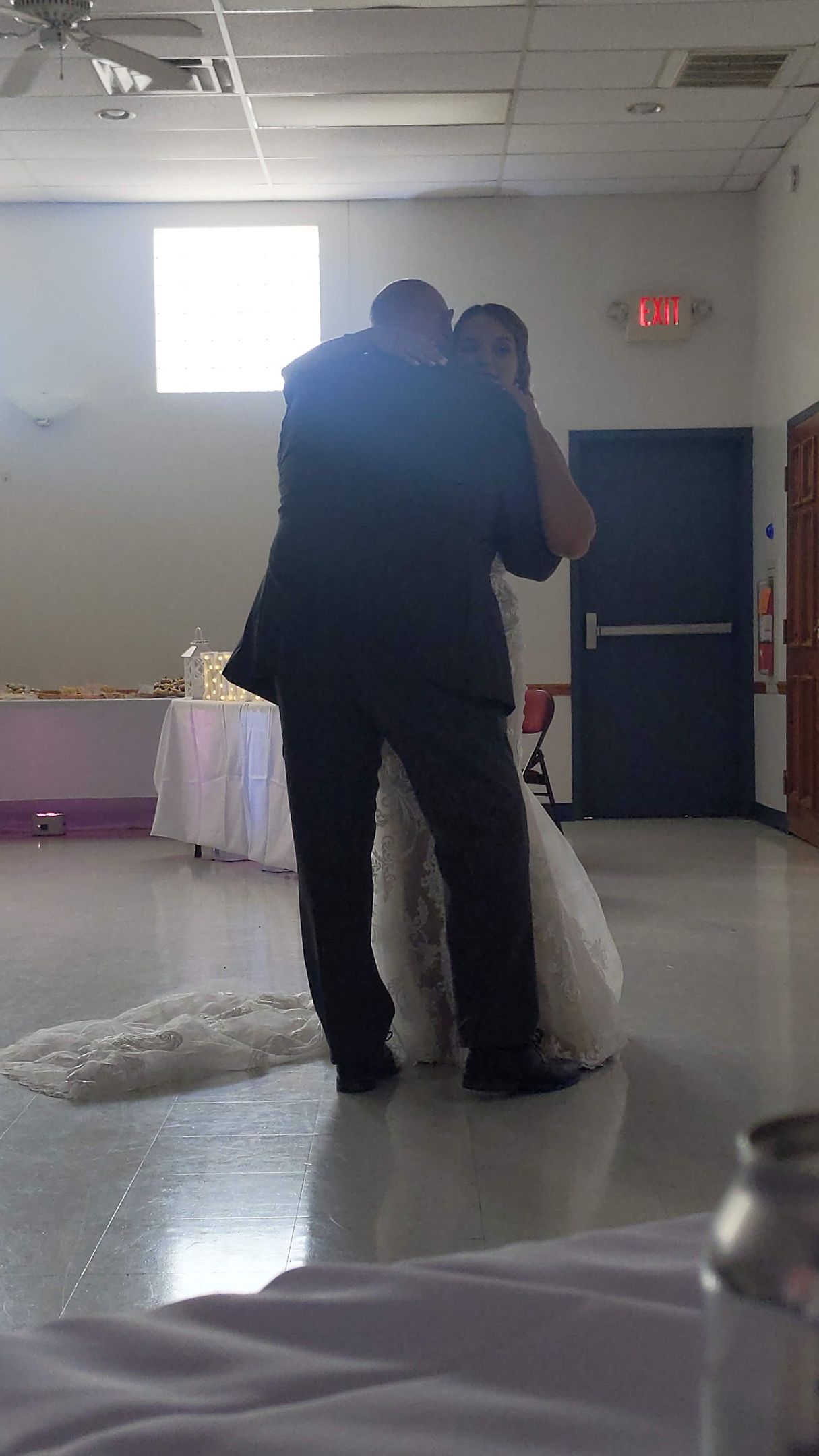 Couple embracing on a dance floor in a decorated hall with a bright window and blue door in the background