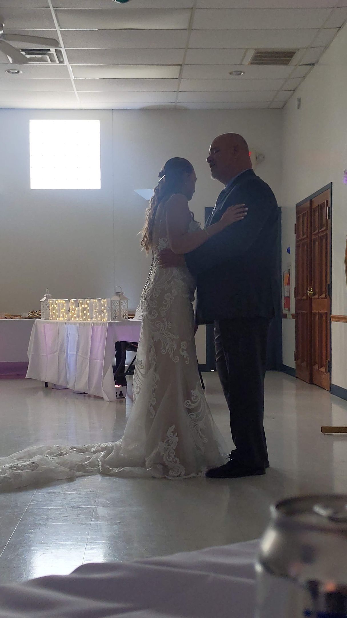 Bride and groom dancing in a reception hall, with a long white gown and bright window light