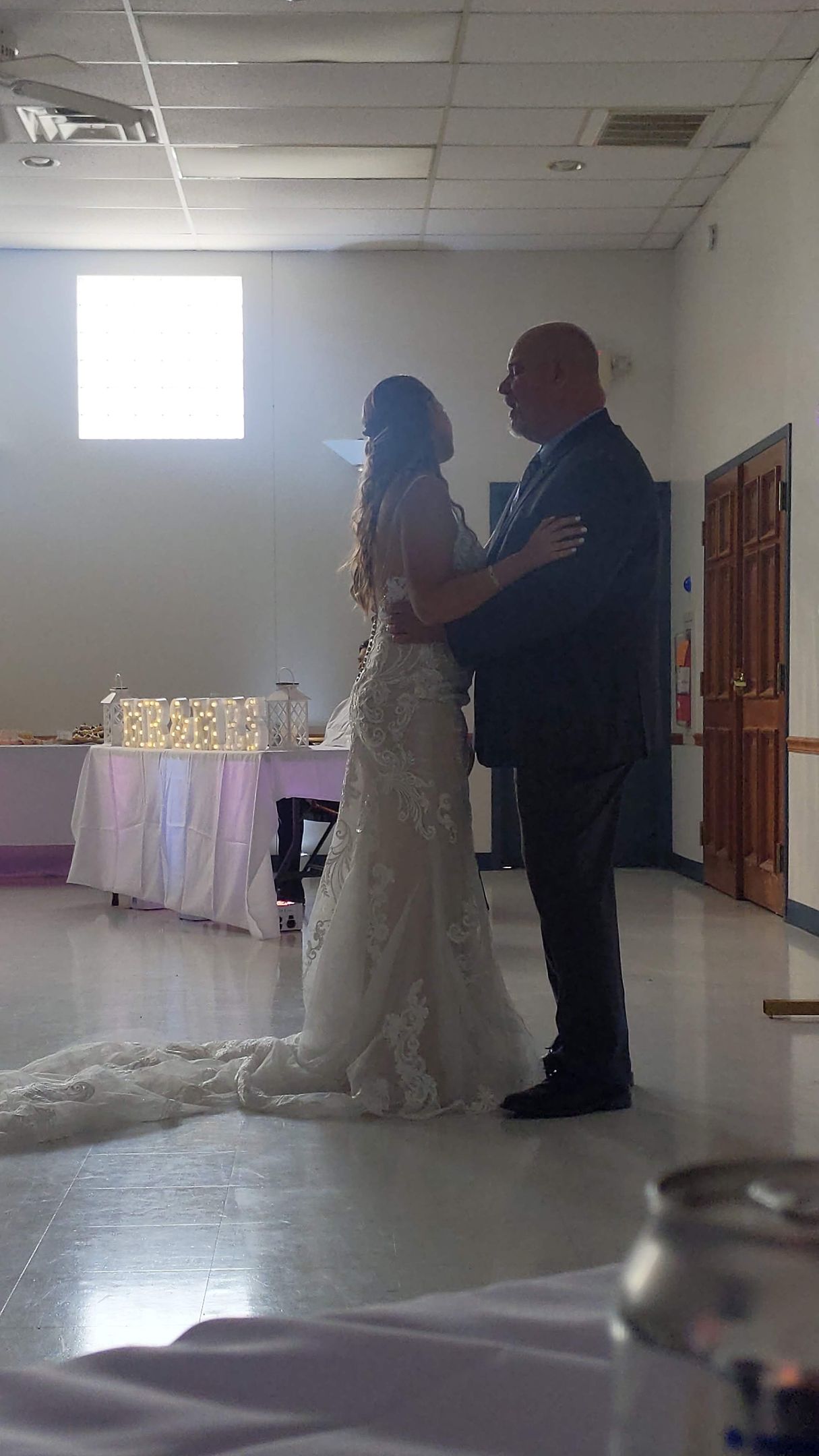 Bride and groom dancing in a reception hall, with a decorated table in the background