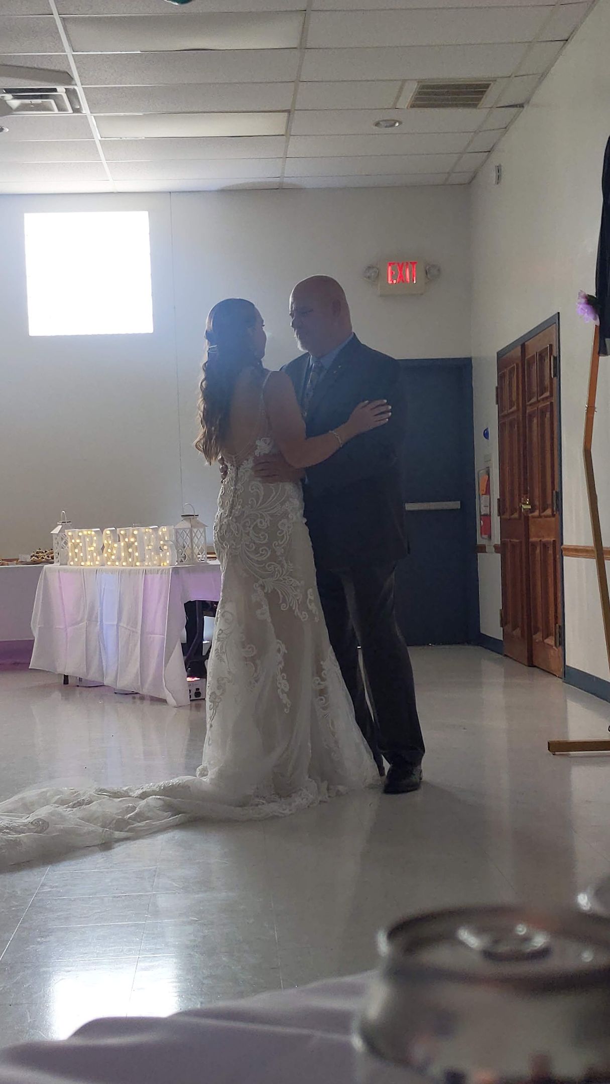 Couple dancing at a wedding reception in a decorated hall with white drapery and soft lighting
