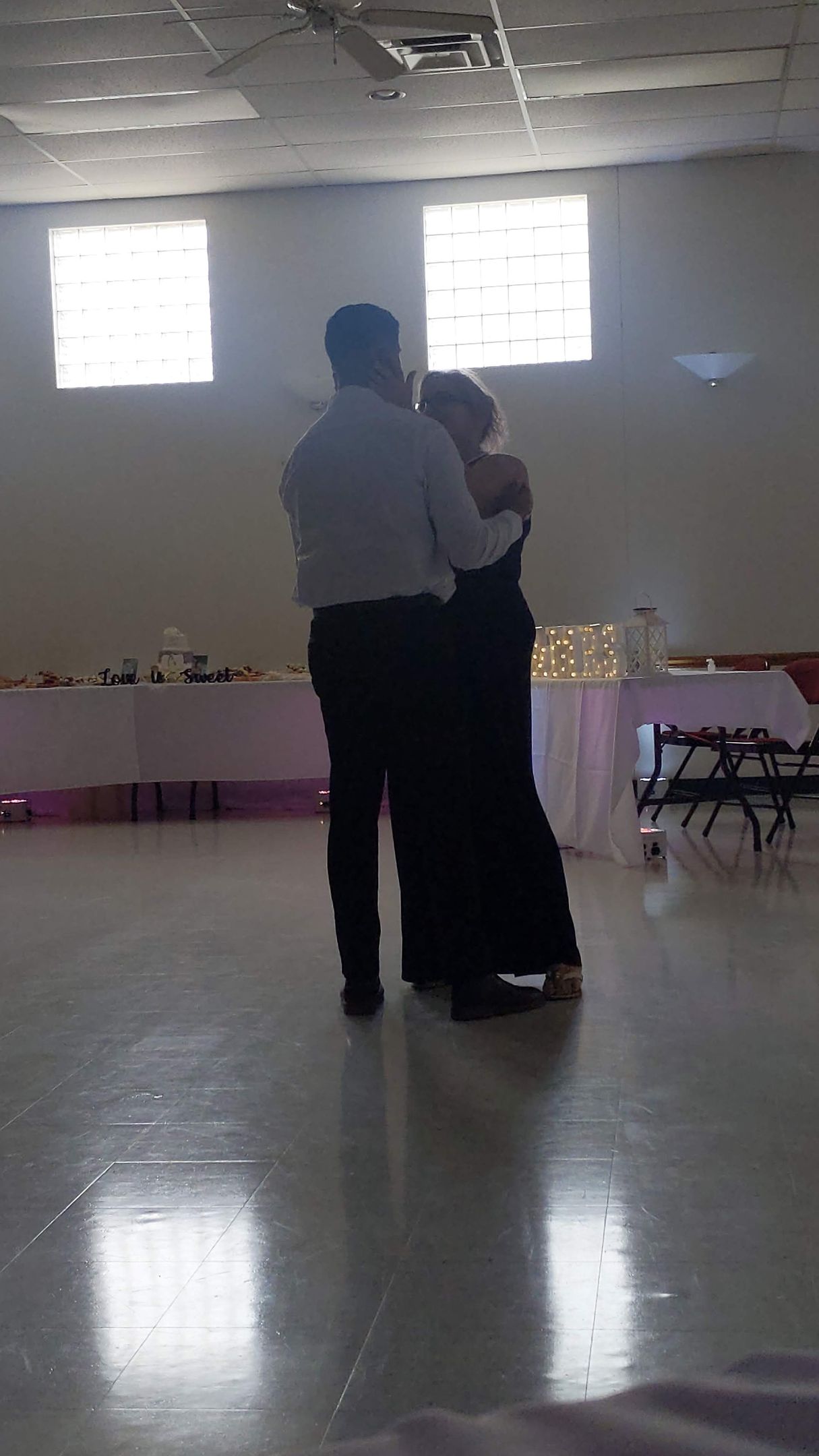 Two people dancing in a bright hall with polished floors and high windows.