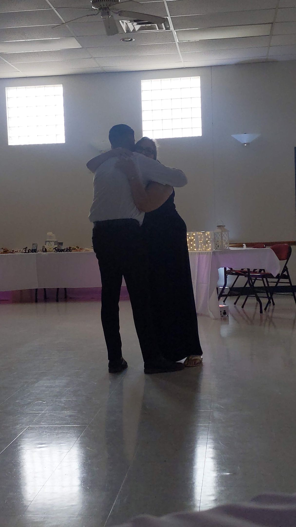 Two people embracing in a bright room with windows and tables along the walls