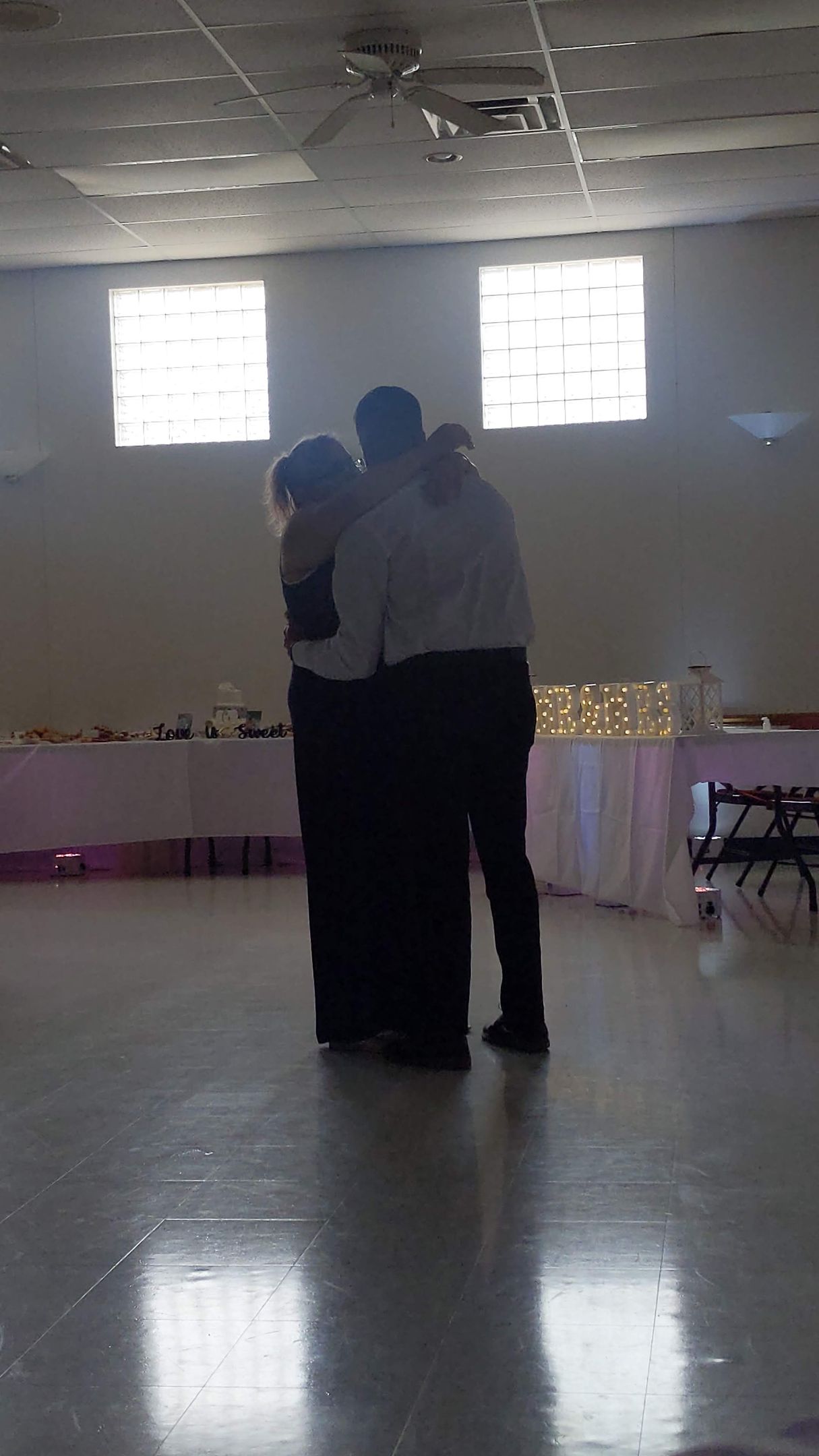 Two people dancing in a dim banquet hall with bright windows and reflective floor