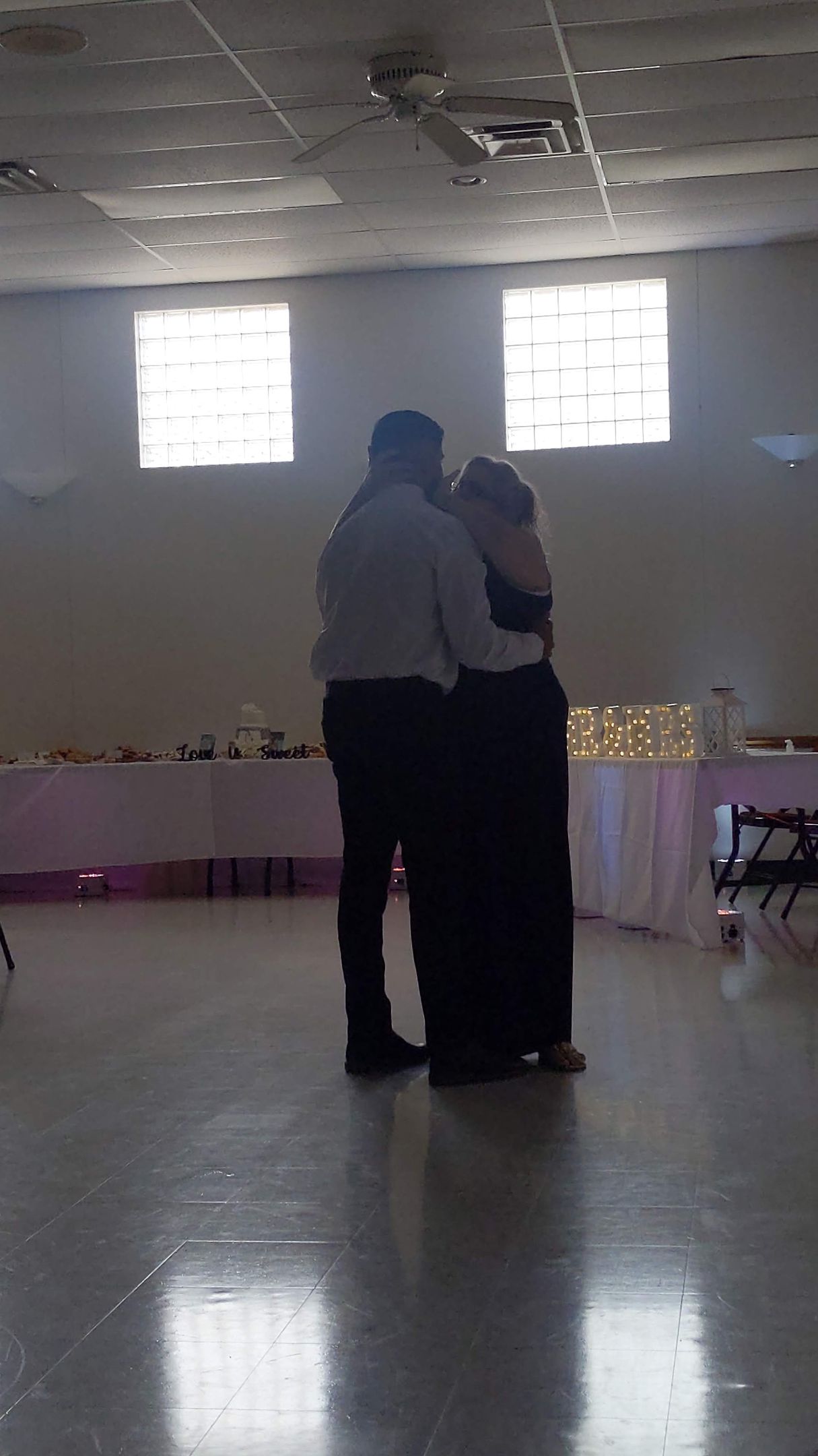 Two people embracing on a dance floor in a decorated hall with soft window light