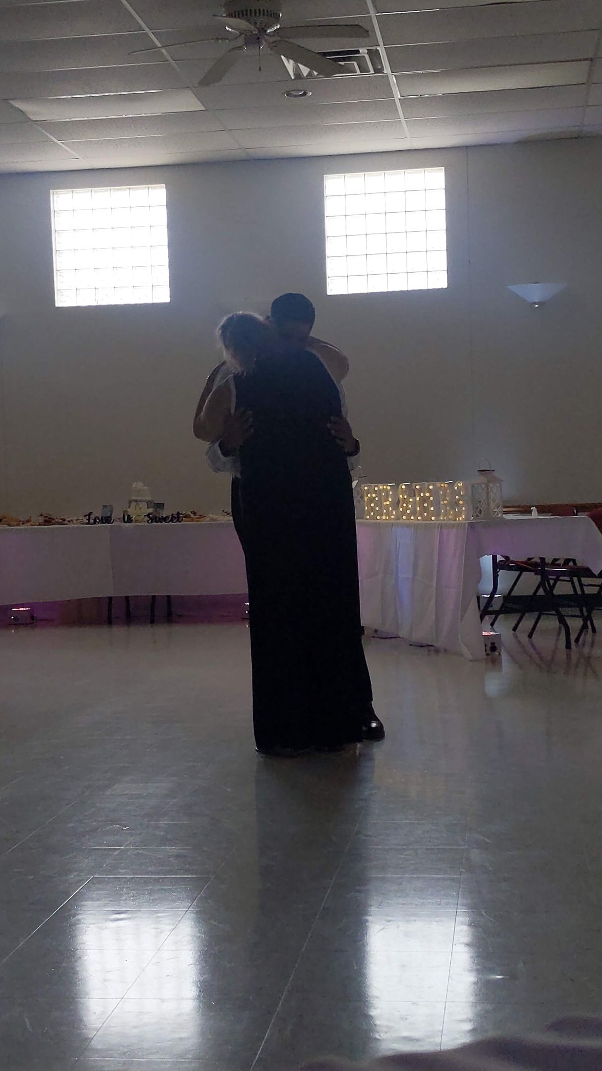 Two people embracing in a large hall with bright windows and a reflective floor