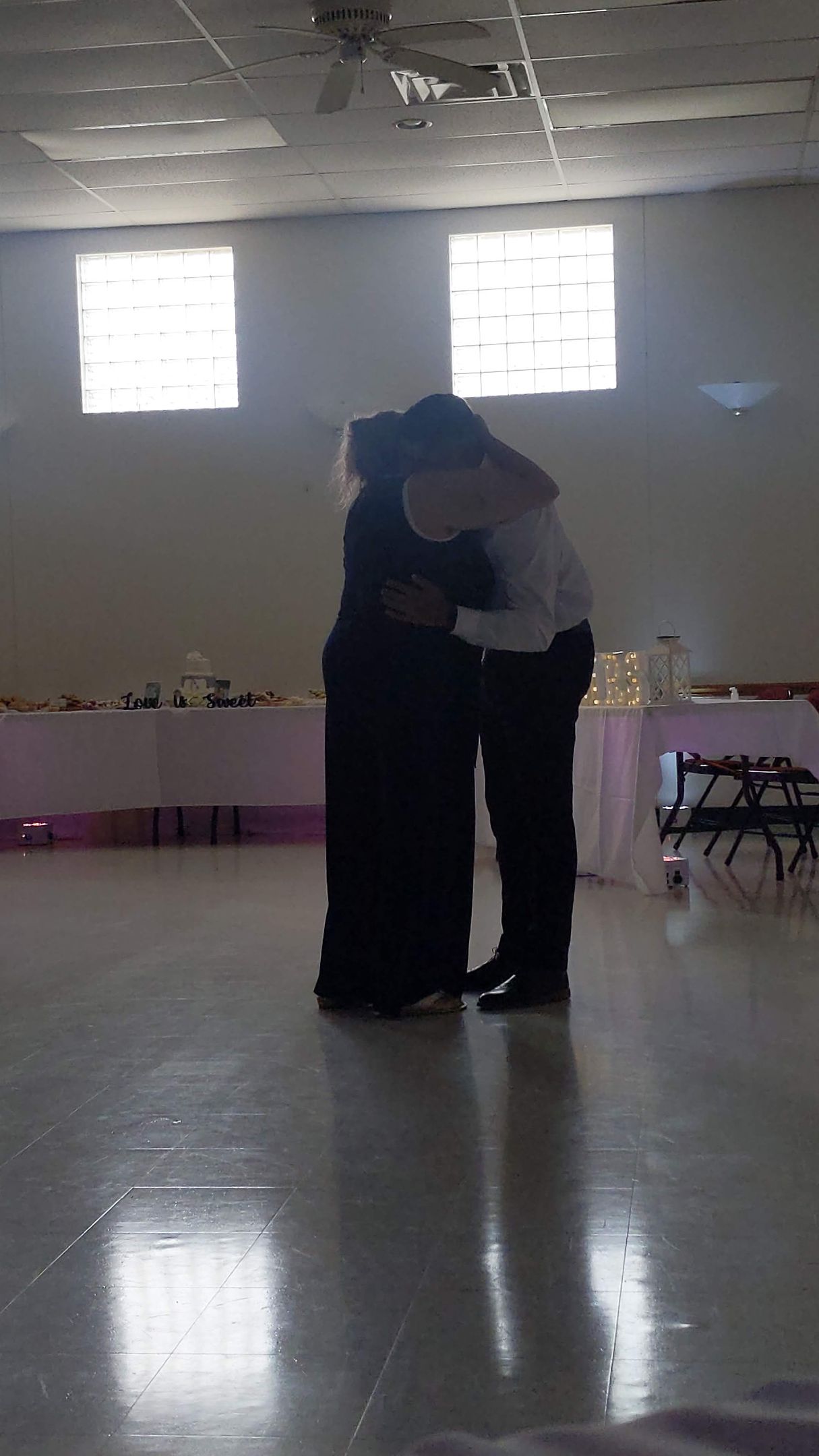 Two people embracing in a bright, empty room with large windows and a glossy floor