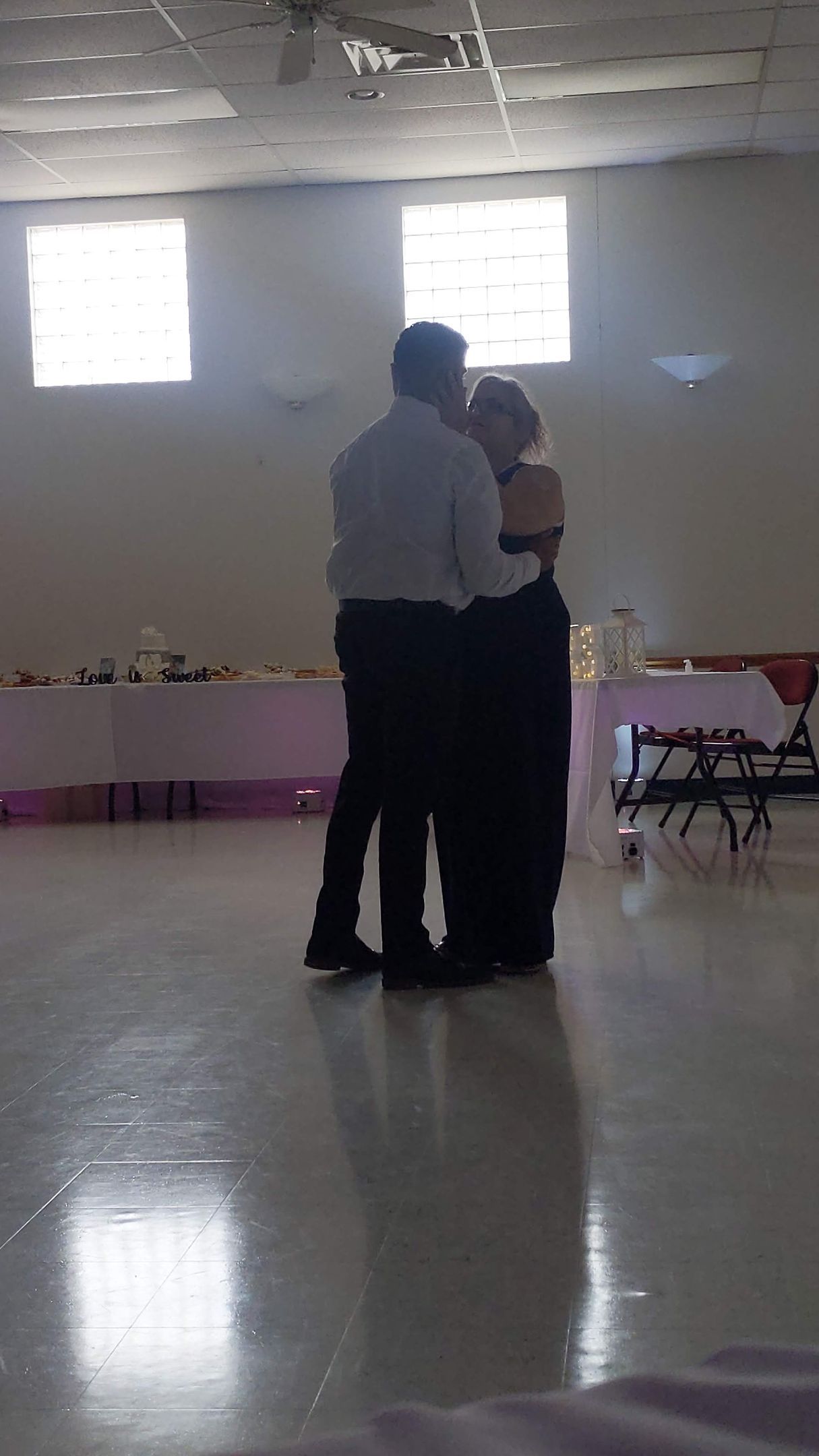 Couple dancing closely in a bright hall with tables along the walls