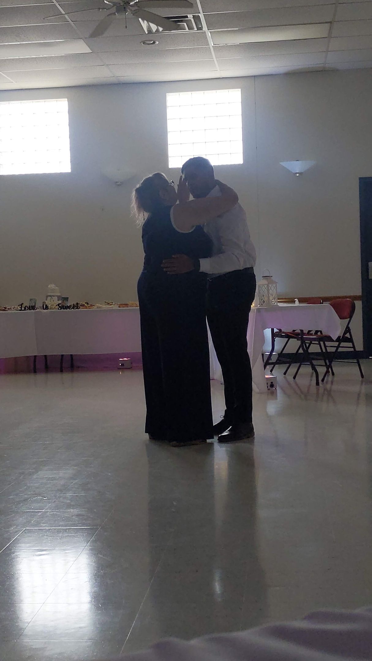 Two people dancing closely in a bright empty room with windows and a glossy floor
