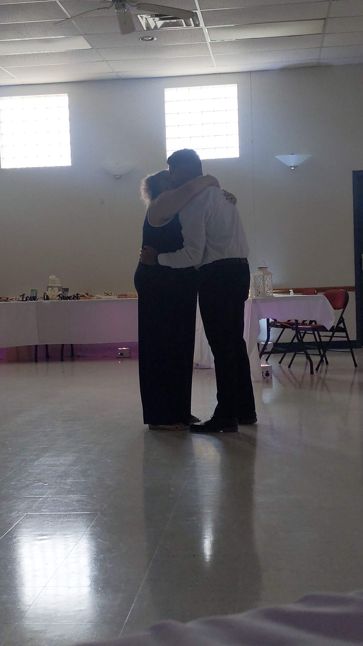 Two people hugging in a bright empty hall with tiled floor and windows