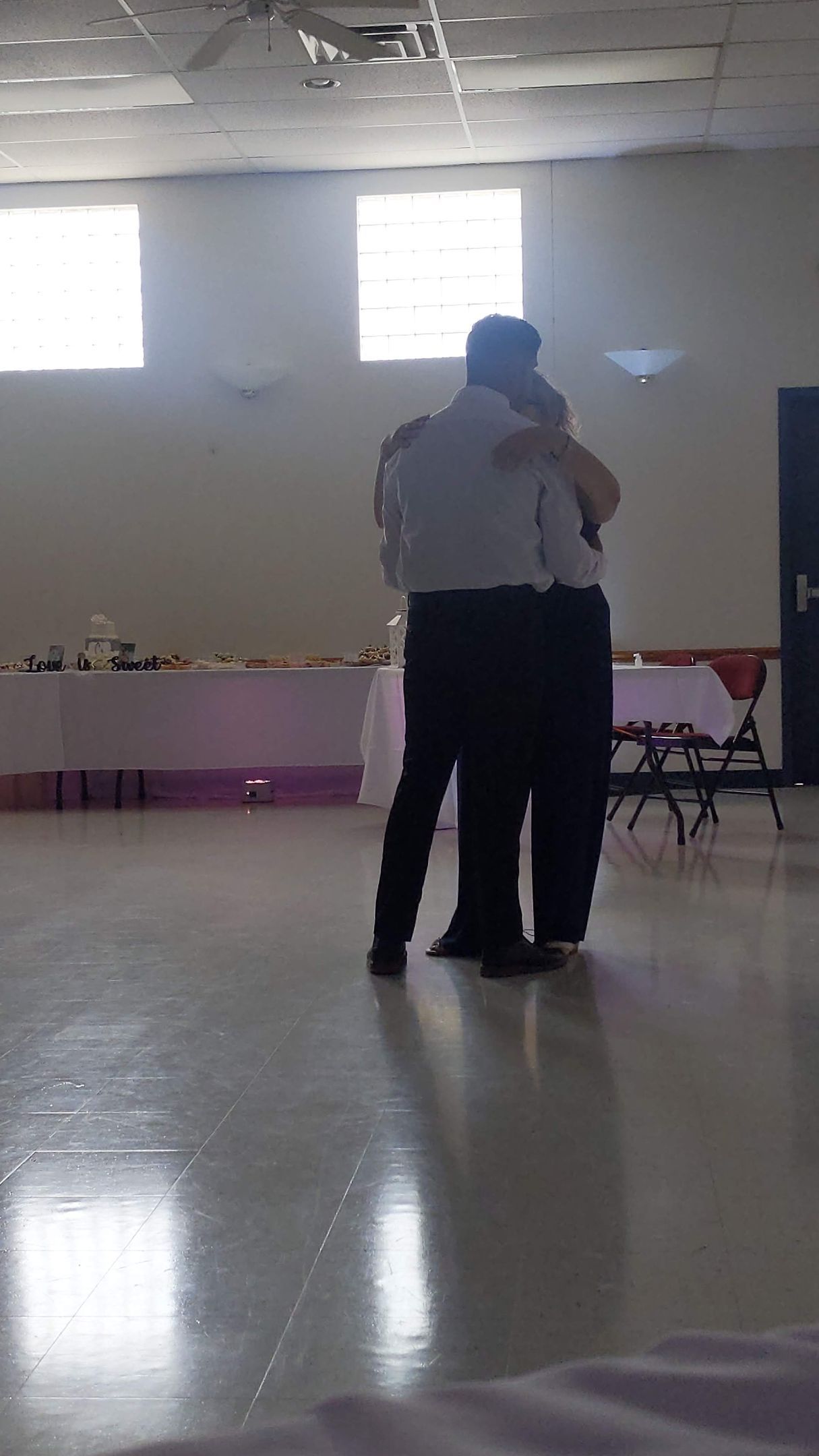 Two people dancing closely in a bright hall with reflective floor and windows