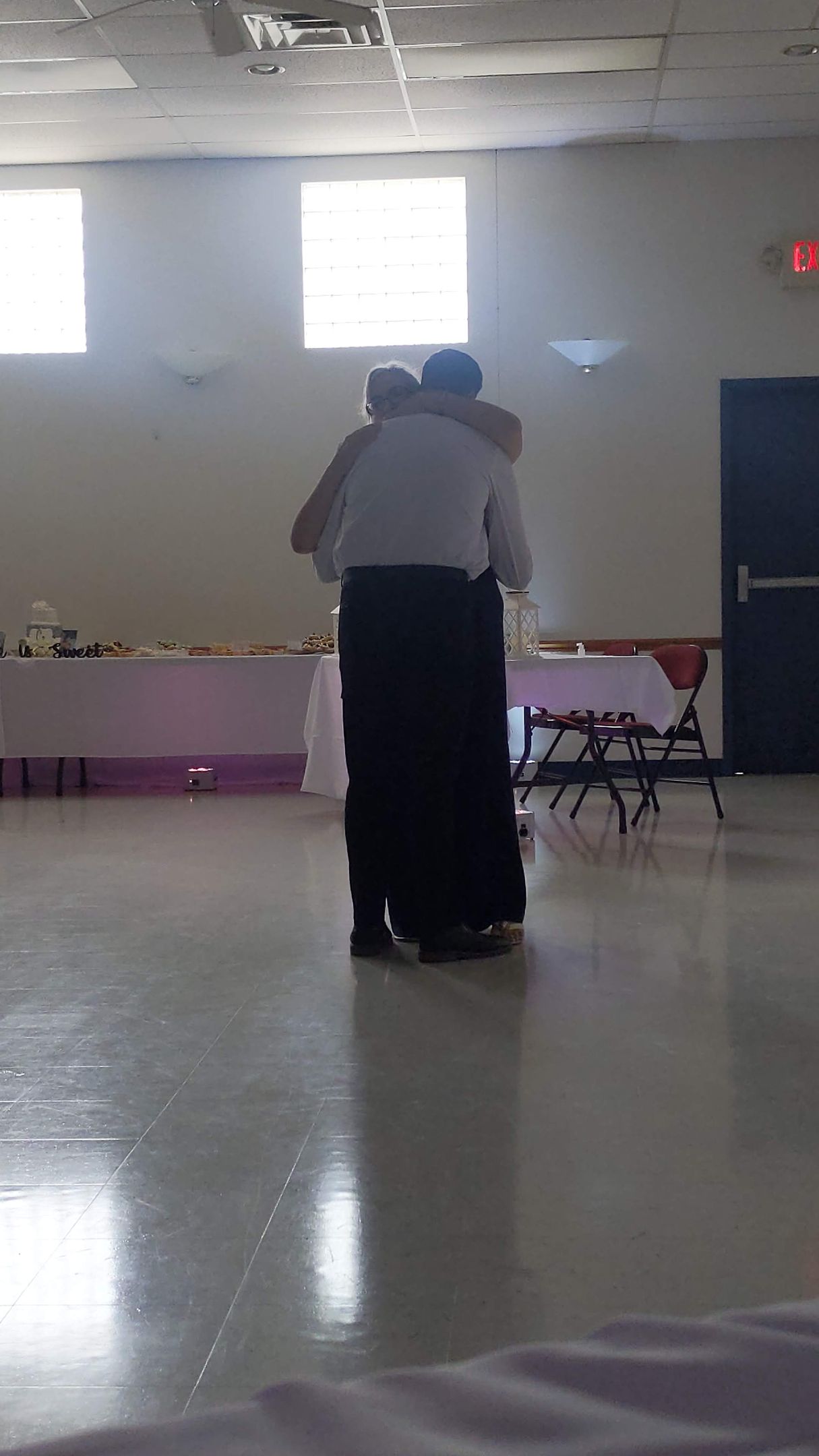 Two people embracing in a bright hall with chairs along the wall