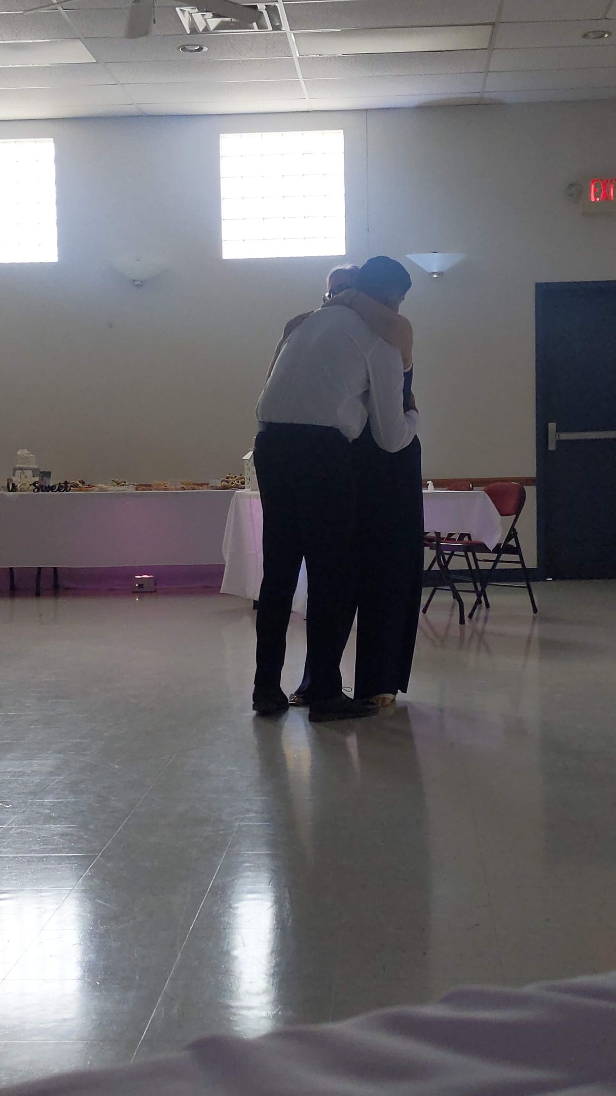 Two people standing close together in a bright hall with tables and a polished floor