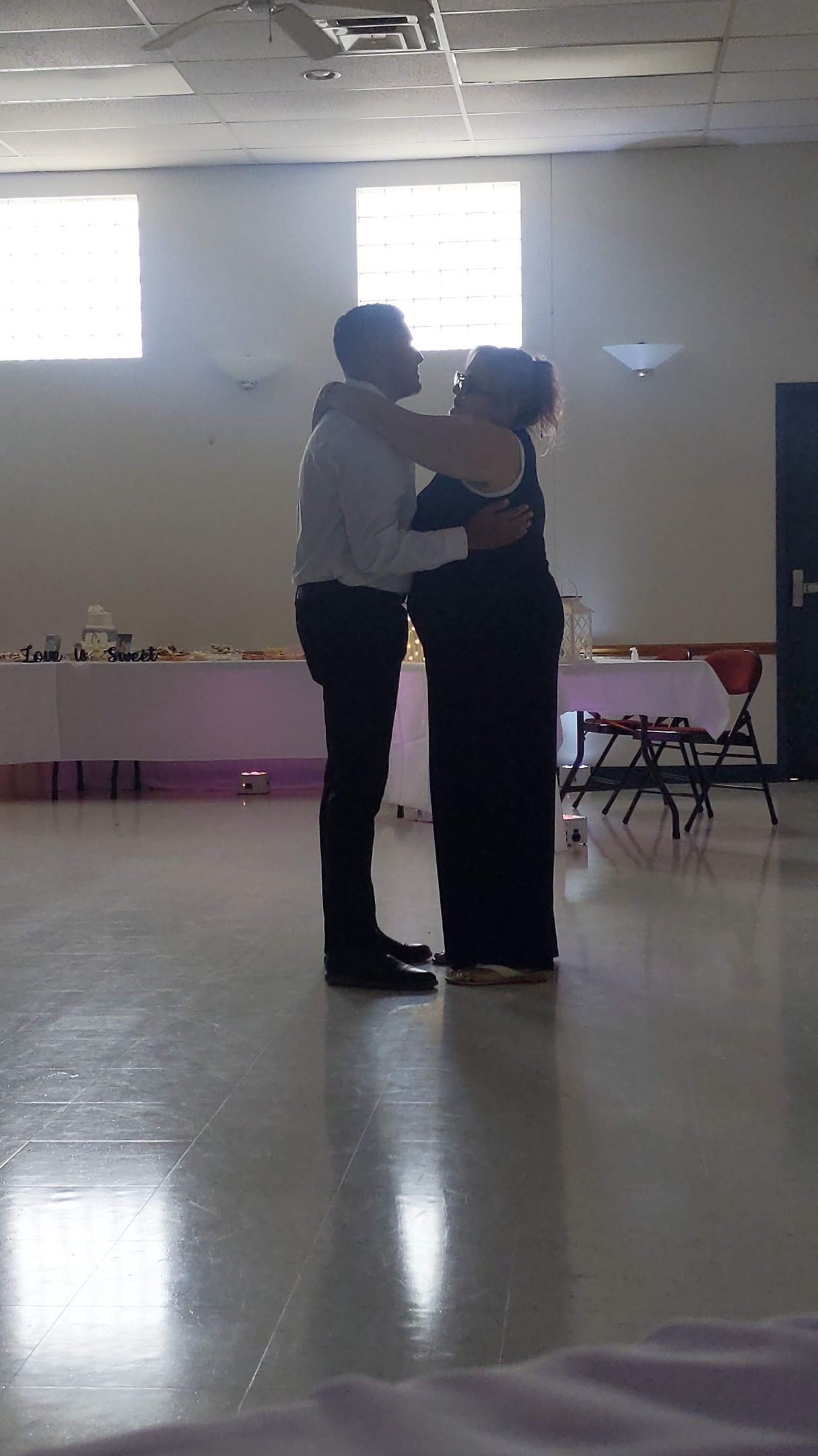 Two people dancing closely in a bright room with tables and windows in the background.