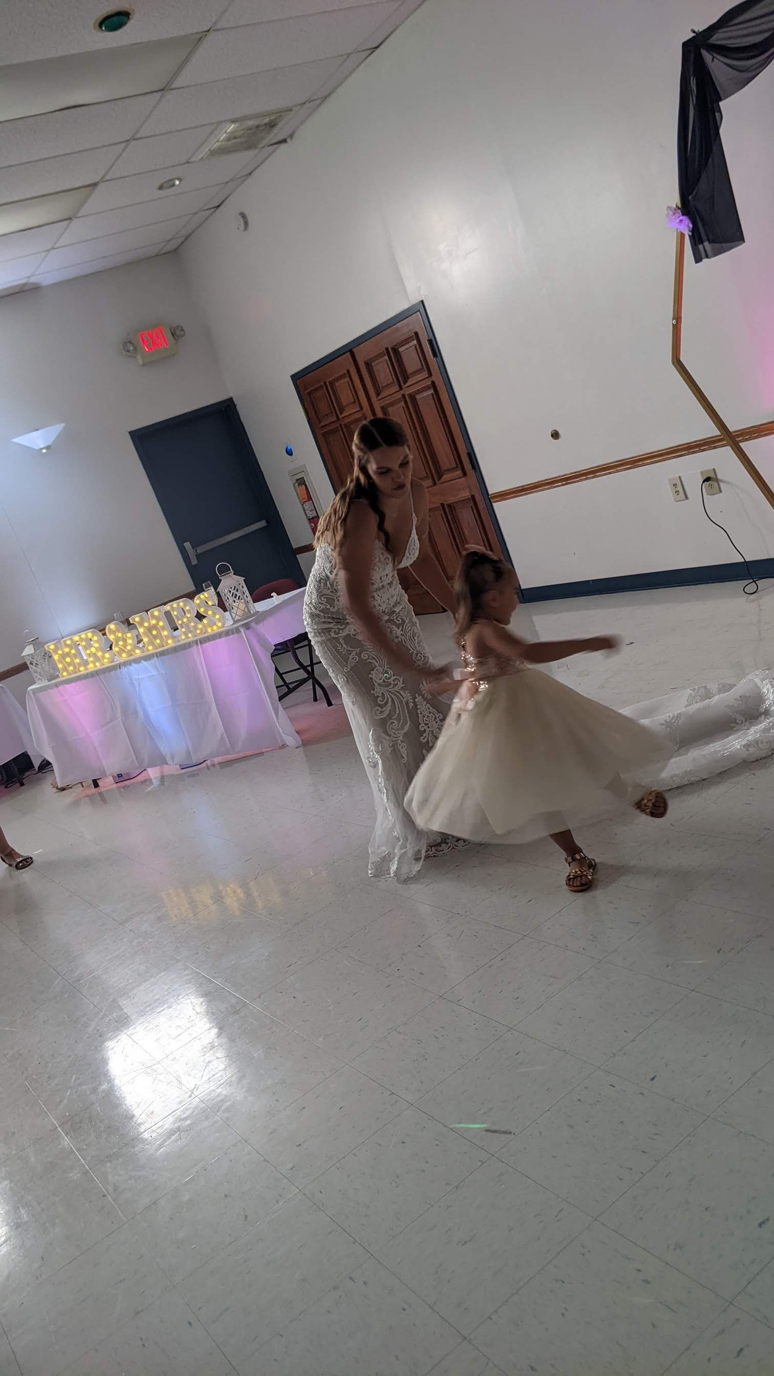 Bride and groom dancing in a decorated banquet hall, with white and purple lighting.