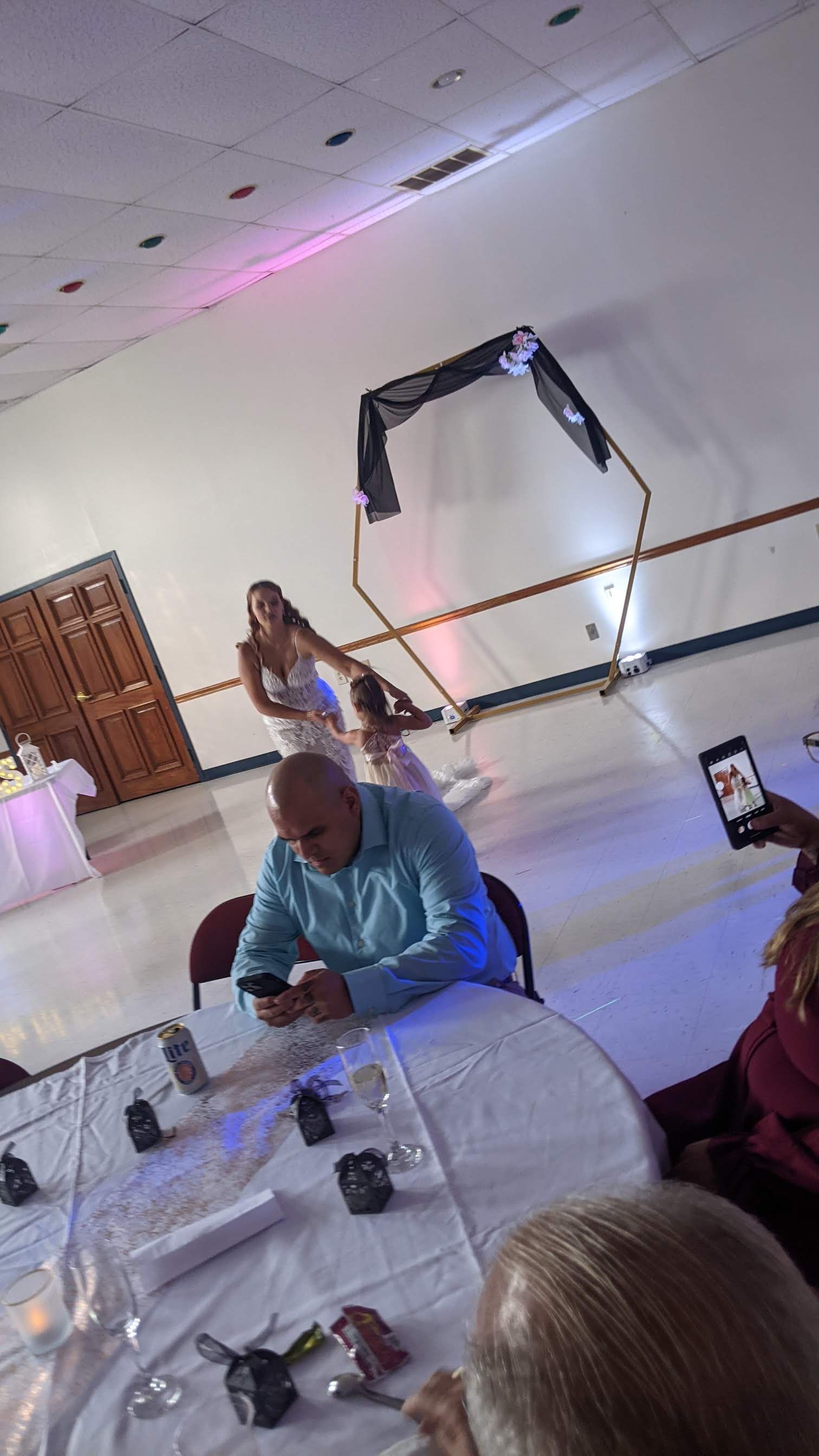 Indoor party scene with white table, seated guests, and pink-lit wall decor.