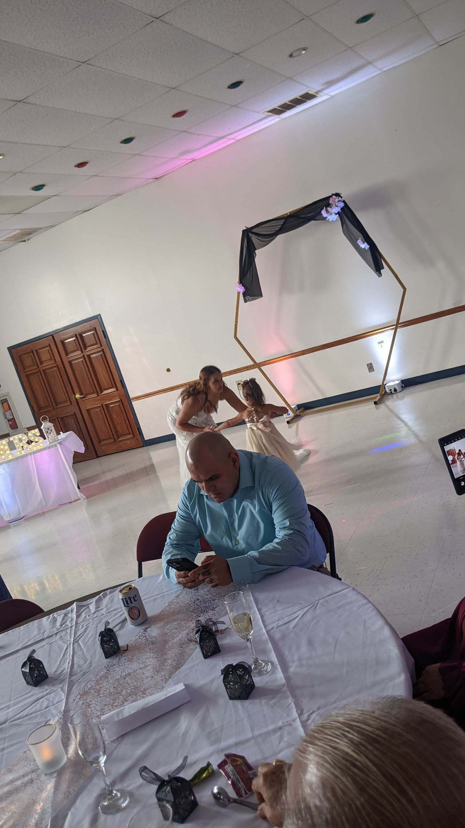 Decorated banquet hall with a seated guest at a table, black and orange balloons, and pink ceiling lights
