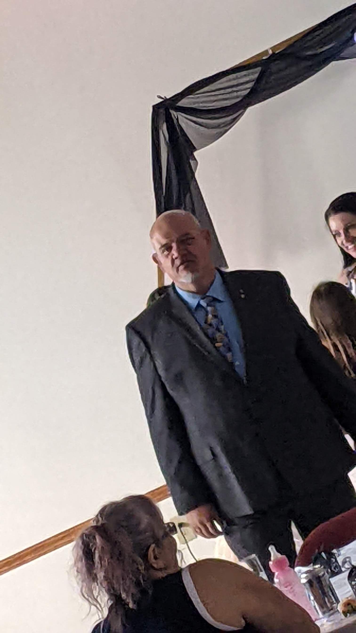 Man in a dark suit standing beside a decorated table at an indoor event