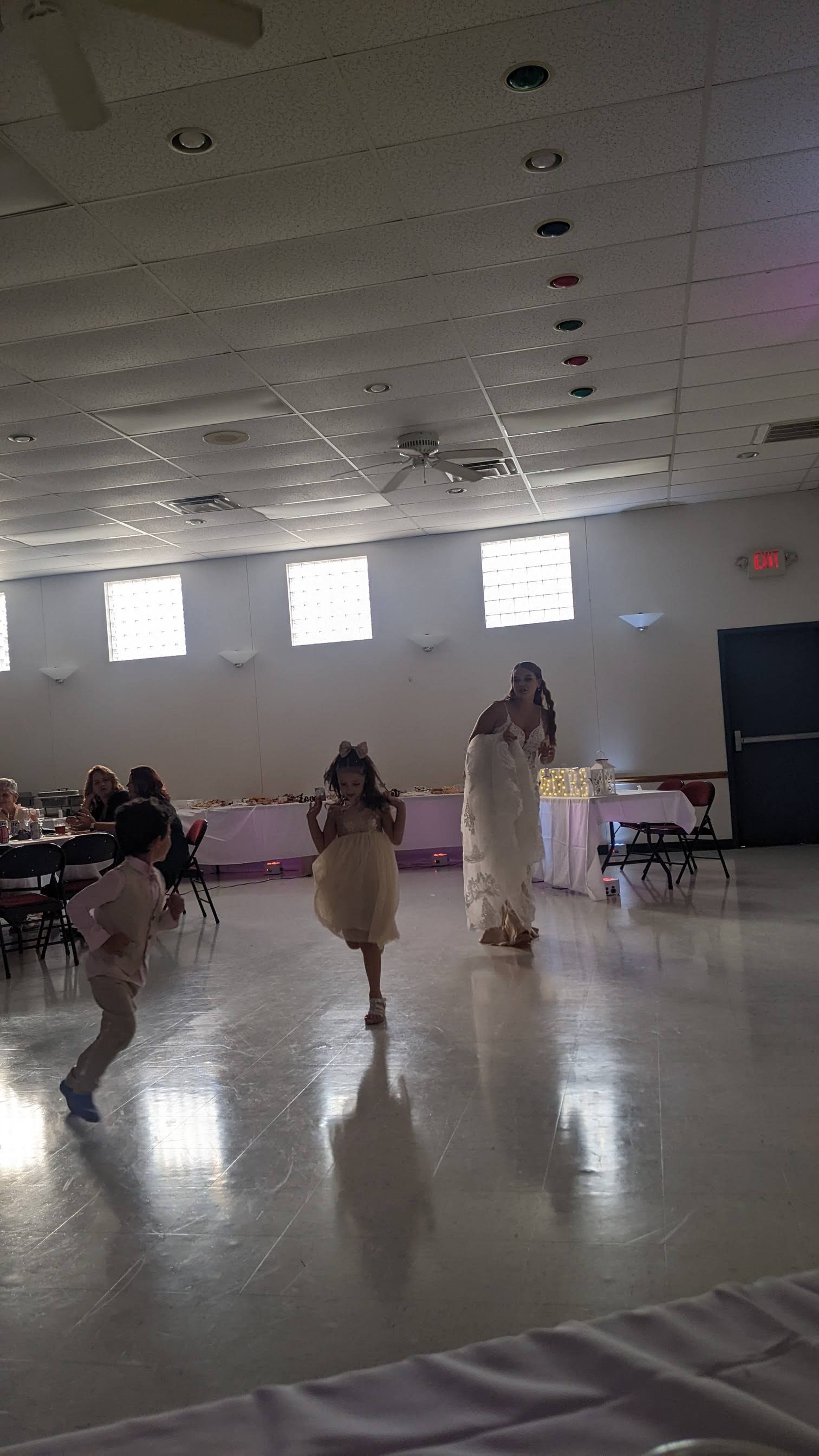 People dancing in a bright hall with tables and chairs along the sides