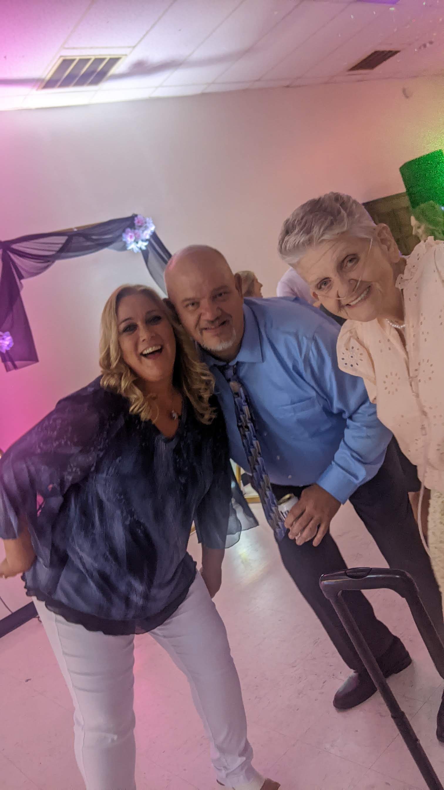 Three people smiling and leaning toward the camera at a party with pink-purple lighting