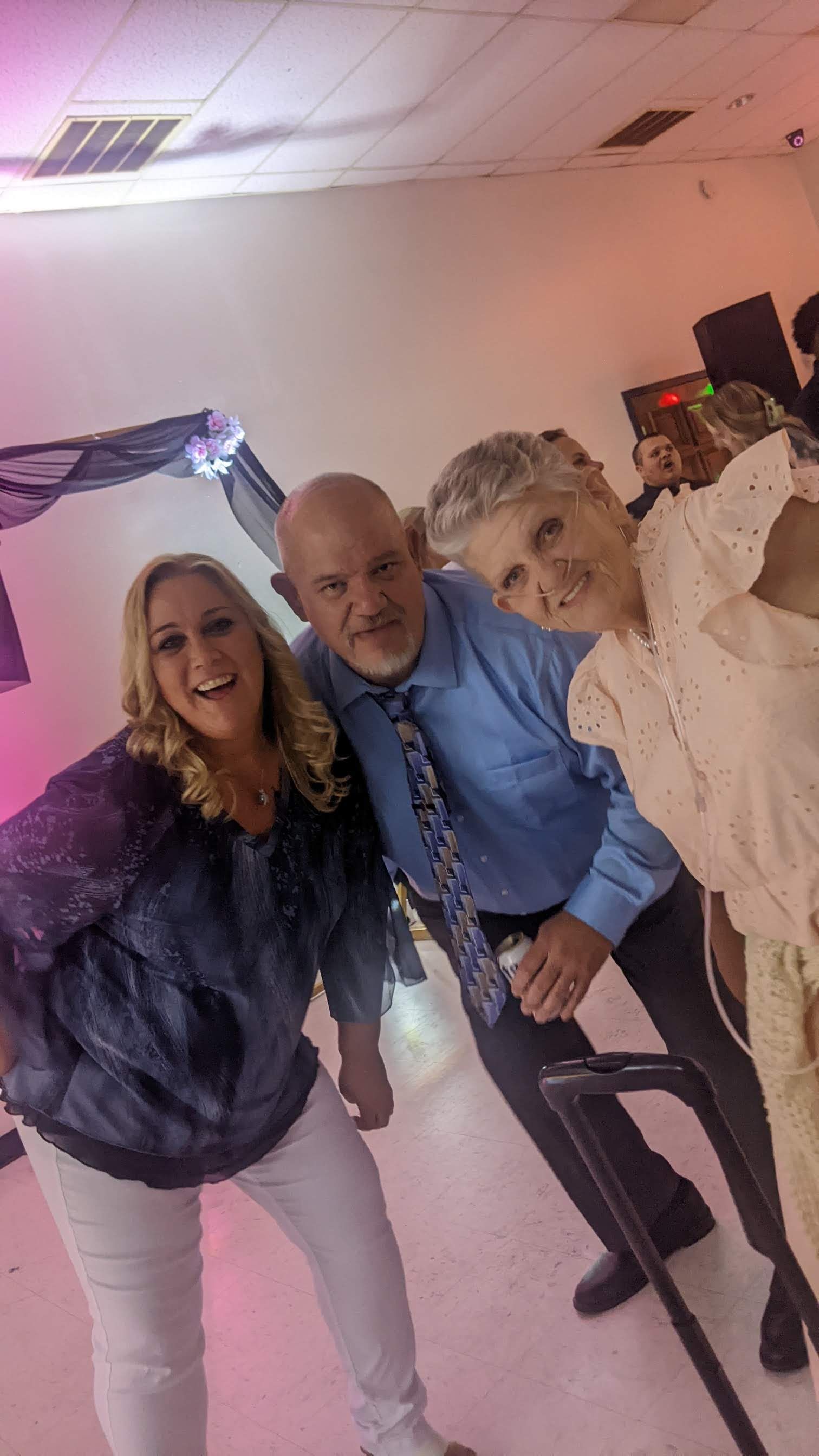 Three people posing indoors at a party, smiling with a pink-lit background.