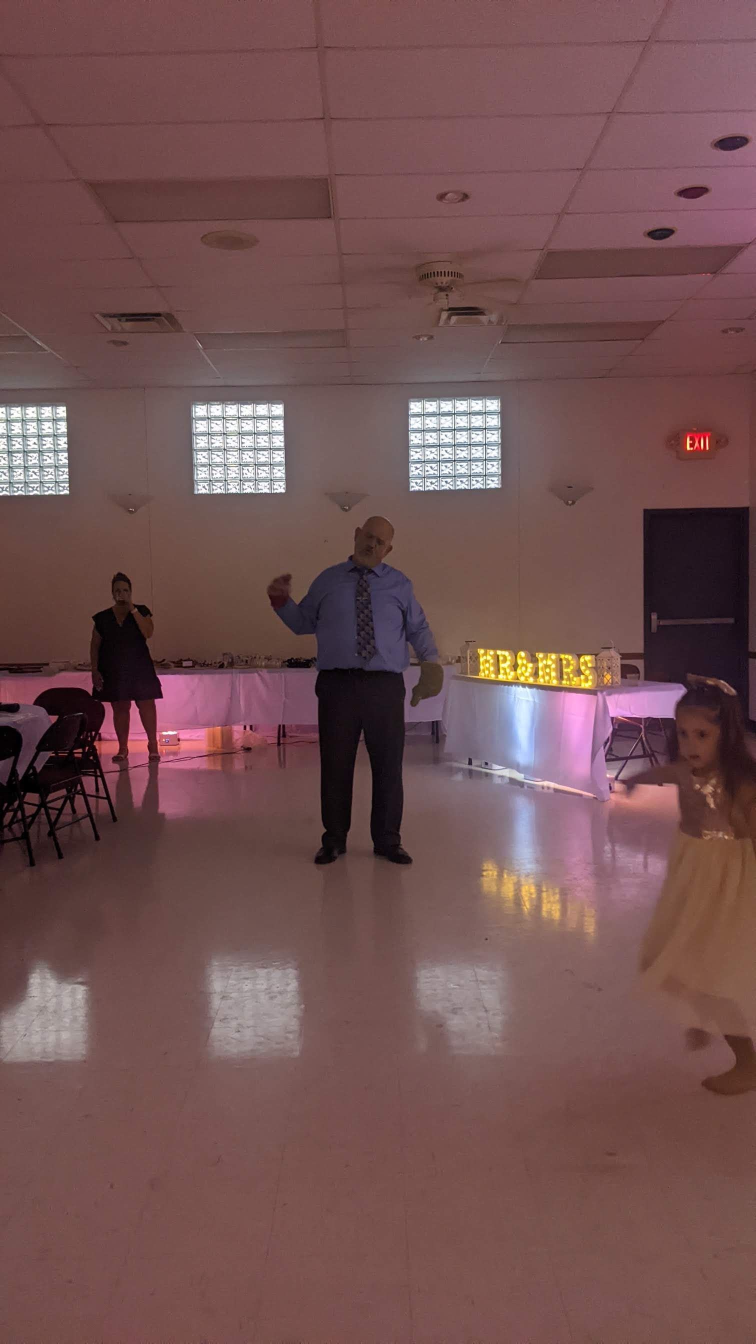 People dancing in a brightly lit hall with pink accent lighting and glass-block windows.