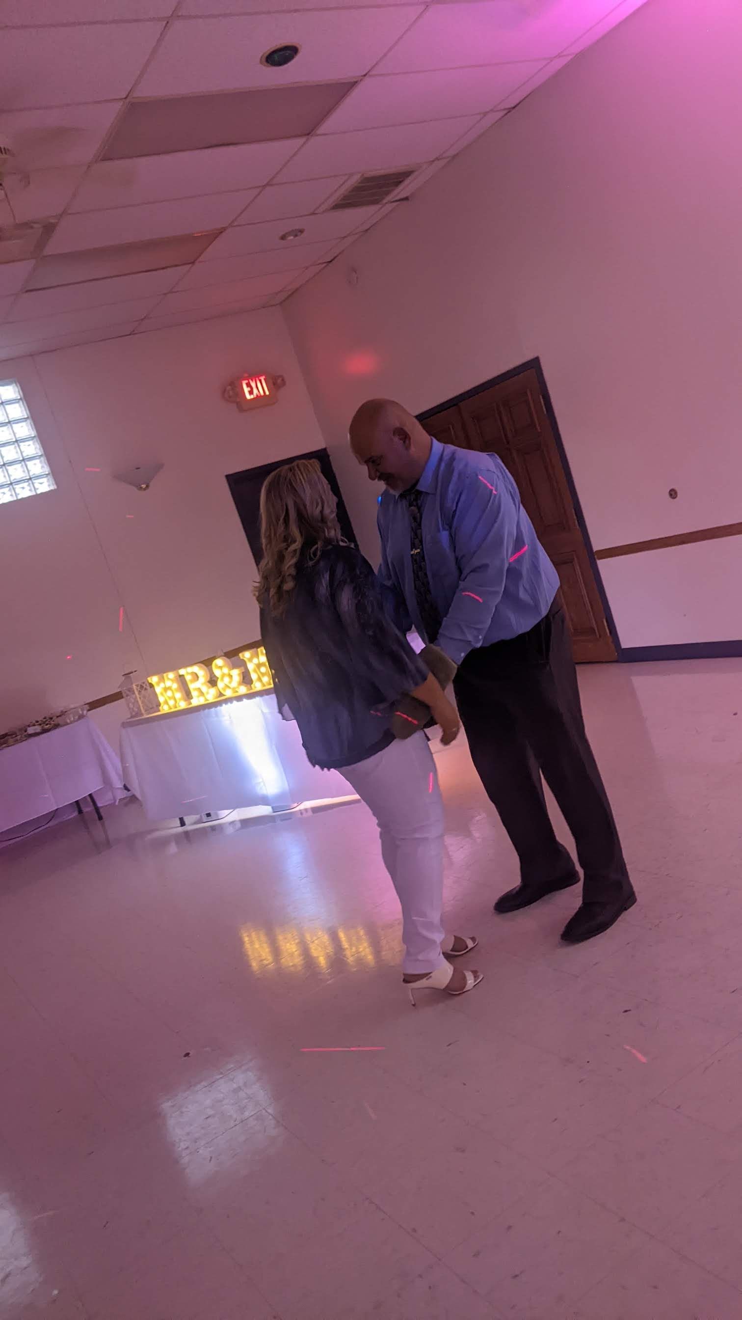 Two people standing in a pink-lit hallway, one leaning in to speak to the other.