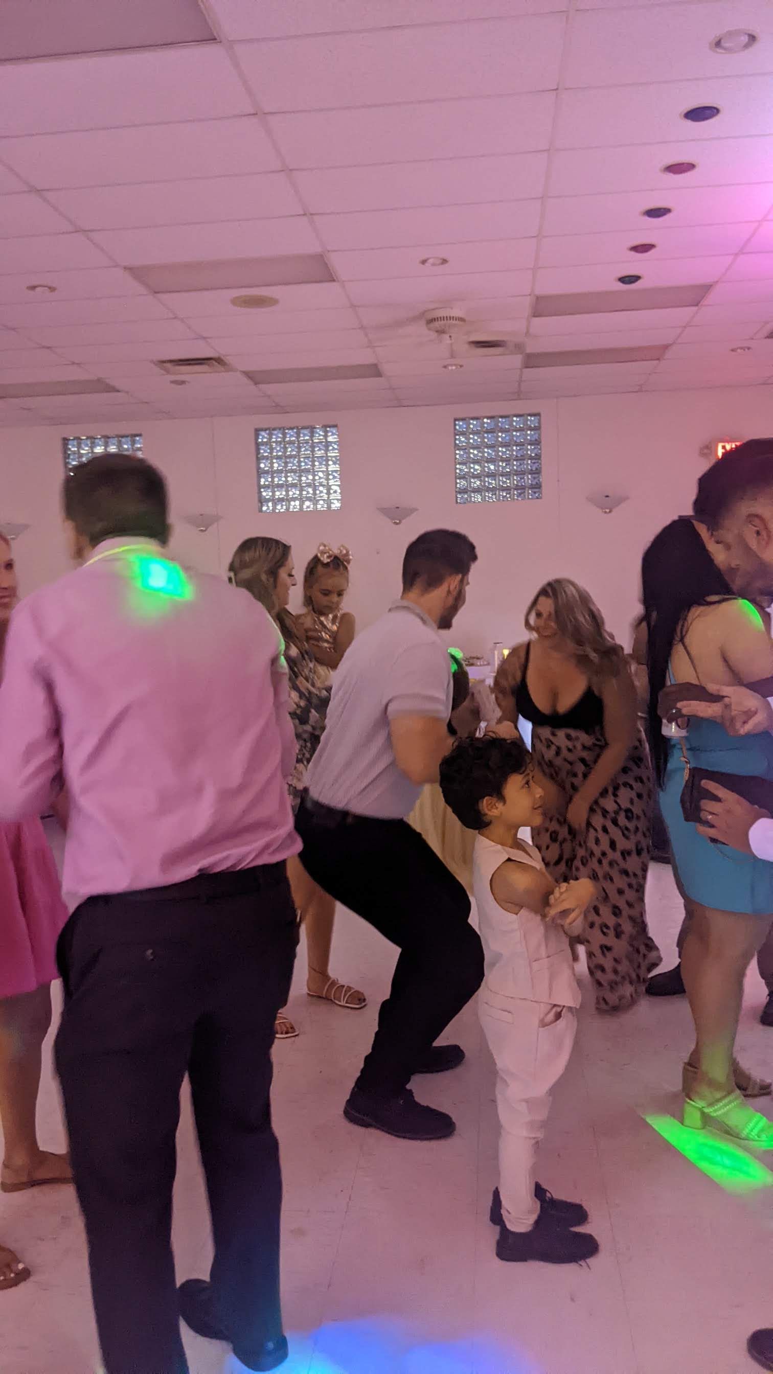 People dancing at a party in a pink-lit room, with a man holding a child on the right.