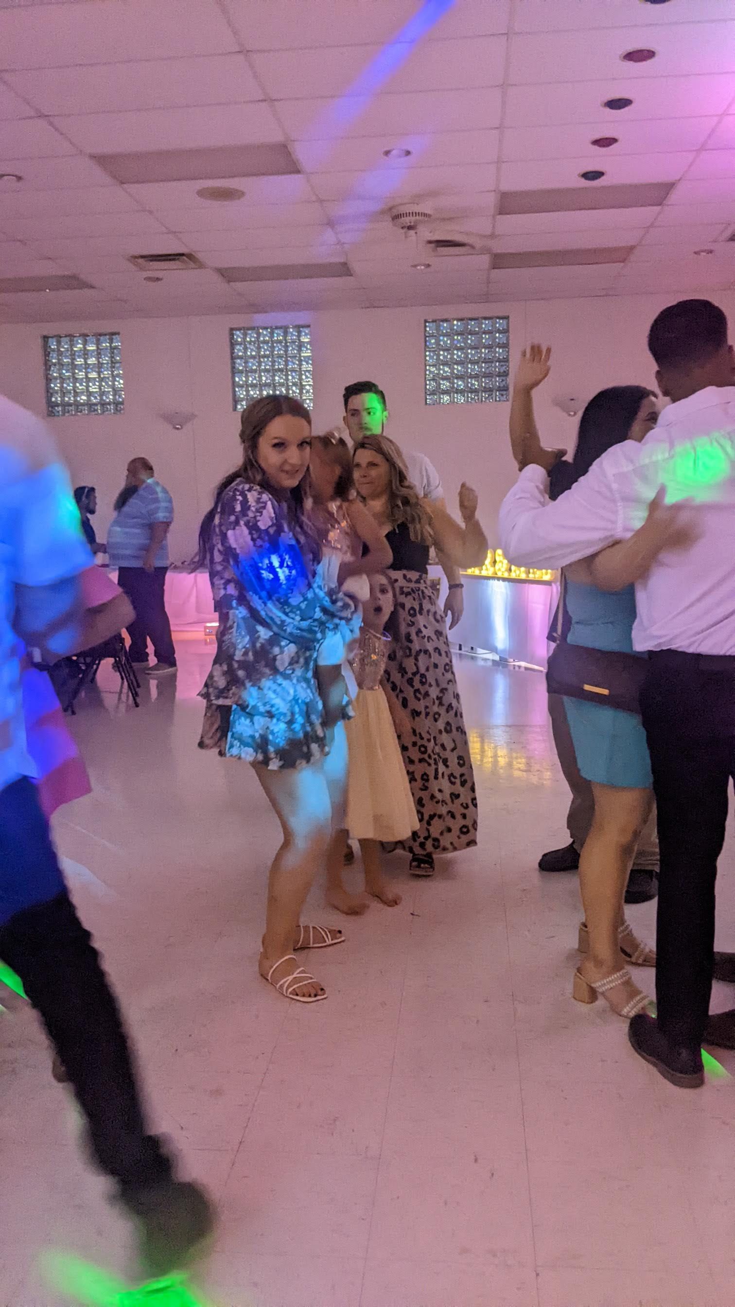 People dancing at a party in a hall with colorful lights.