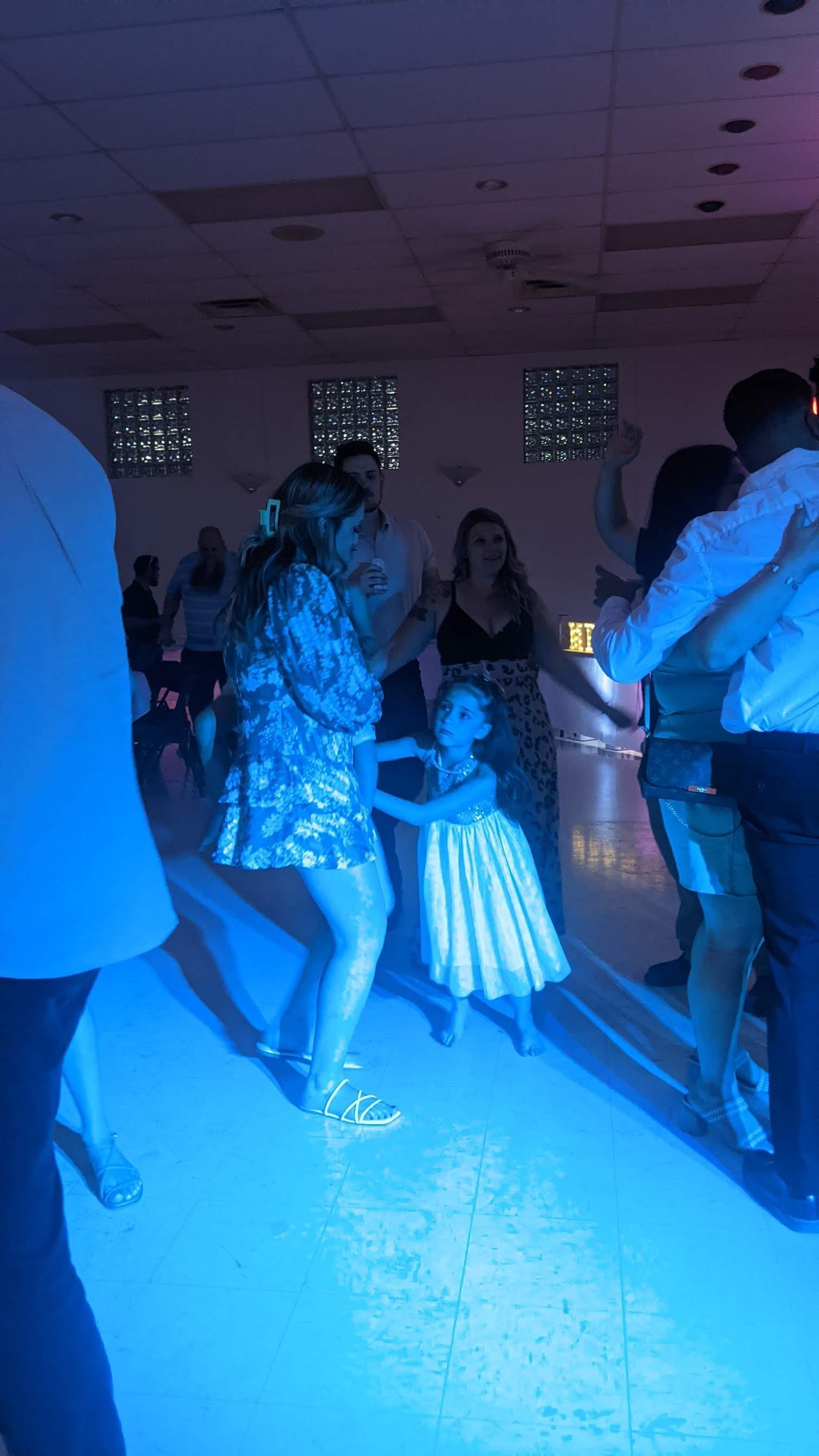 People dancing in a blue-lit indoor party room, with a lit dress in the center.