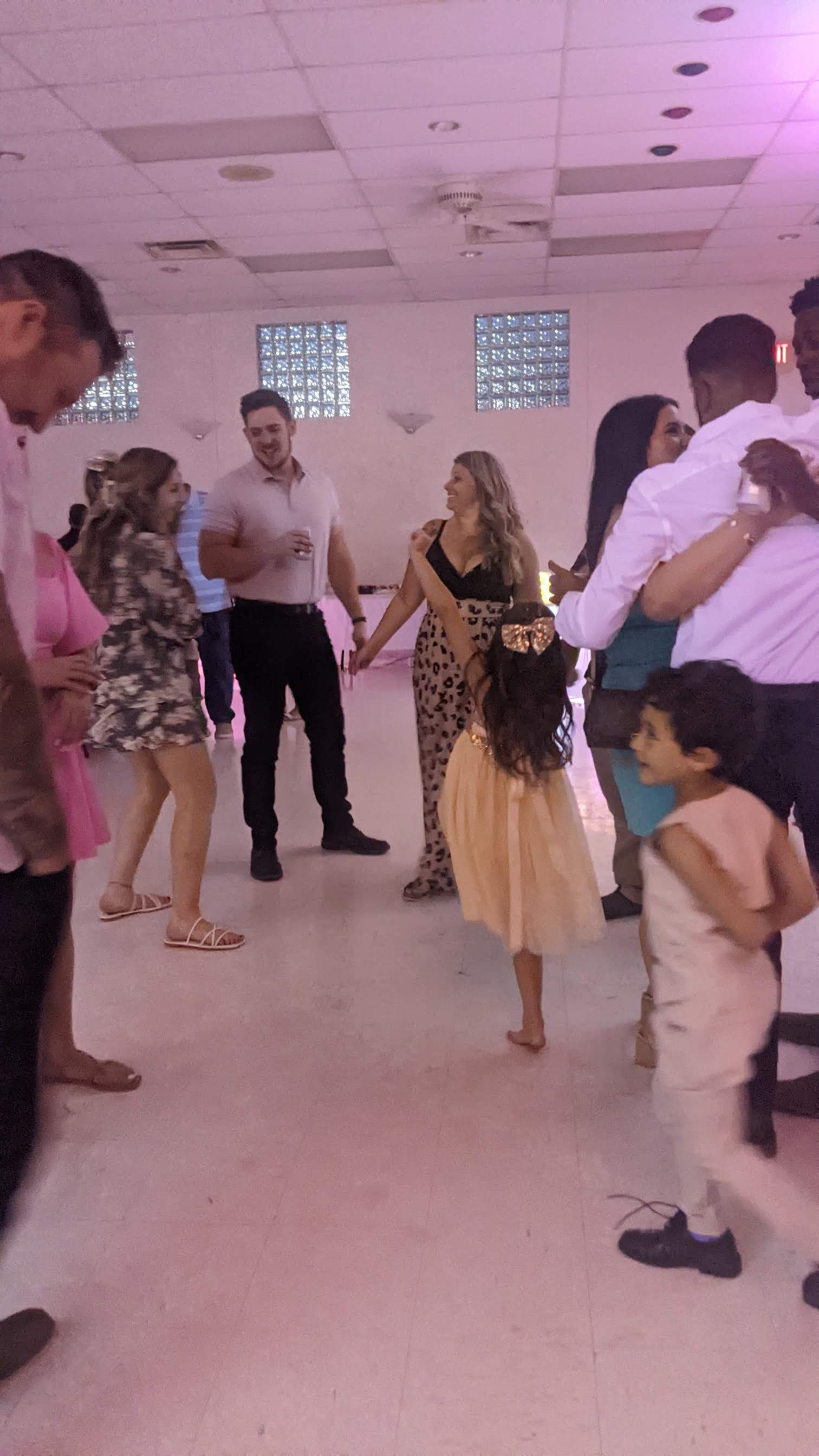 People dancing at a party in a pink-lit room, with a child in the foreground.