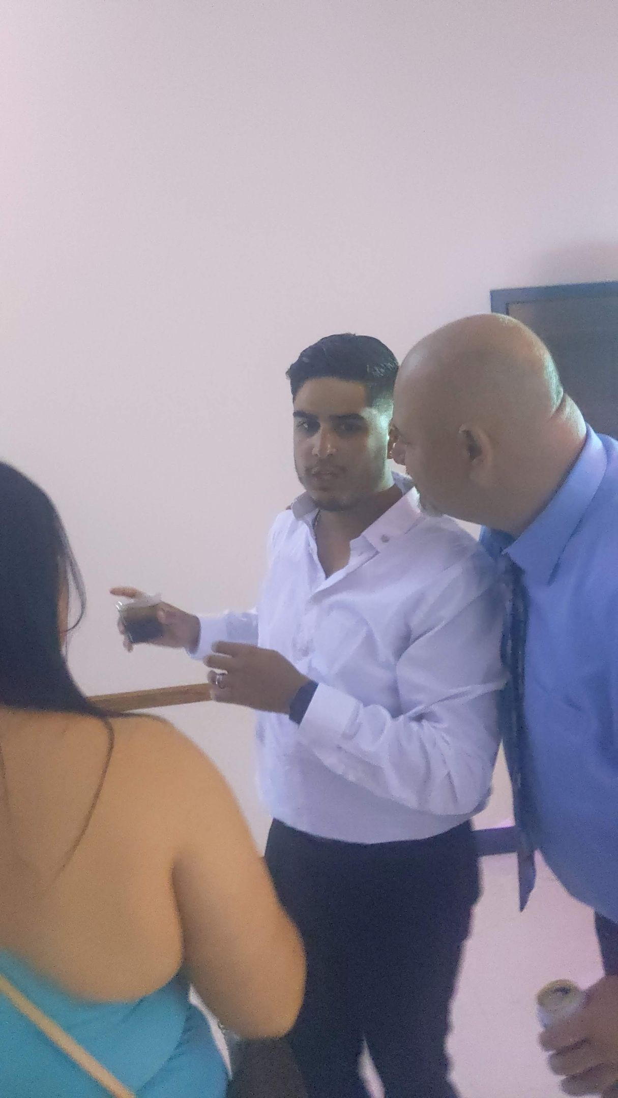 Three people converse indoors; one man points while another leans in to listen.