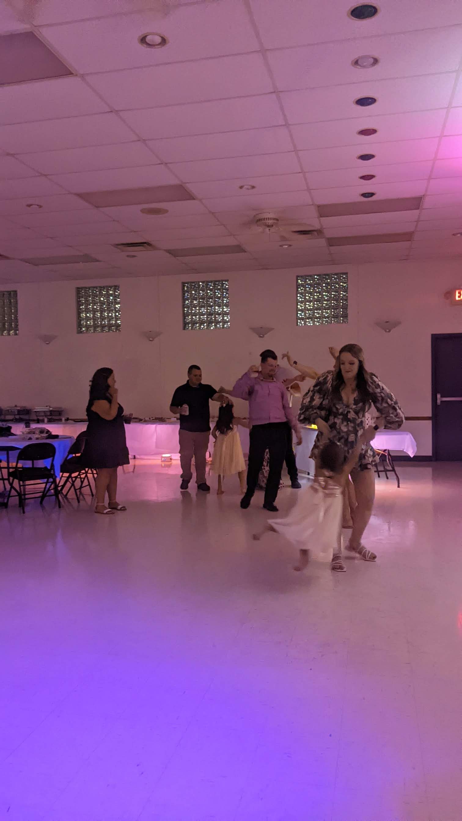 People dancing in a banquet hall with purple lighting and a dance floor