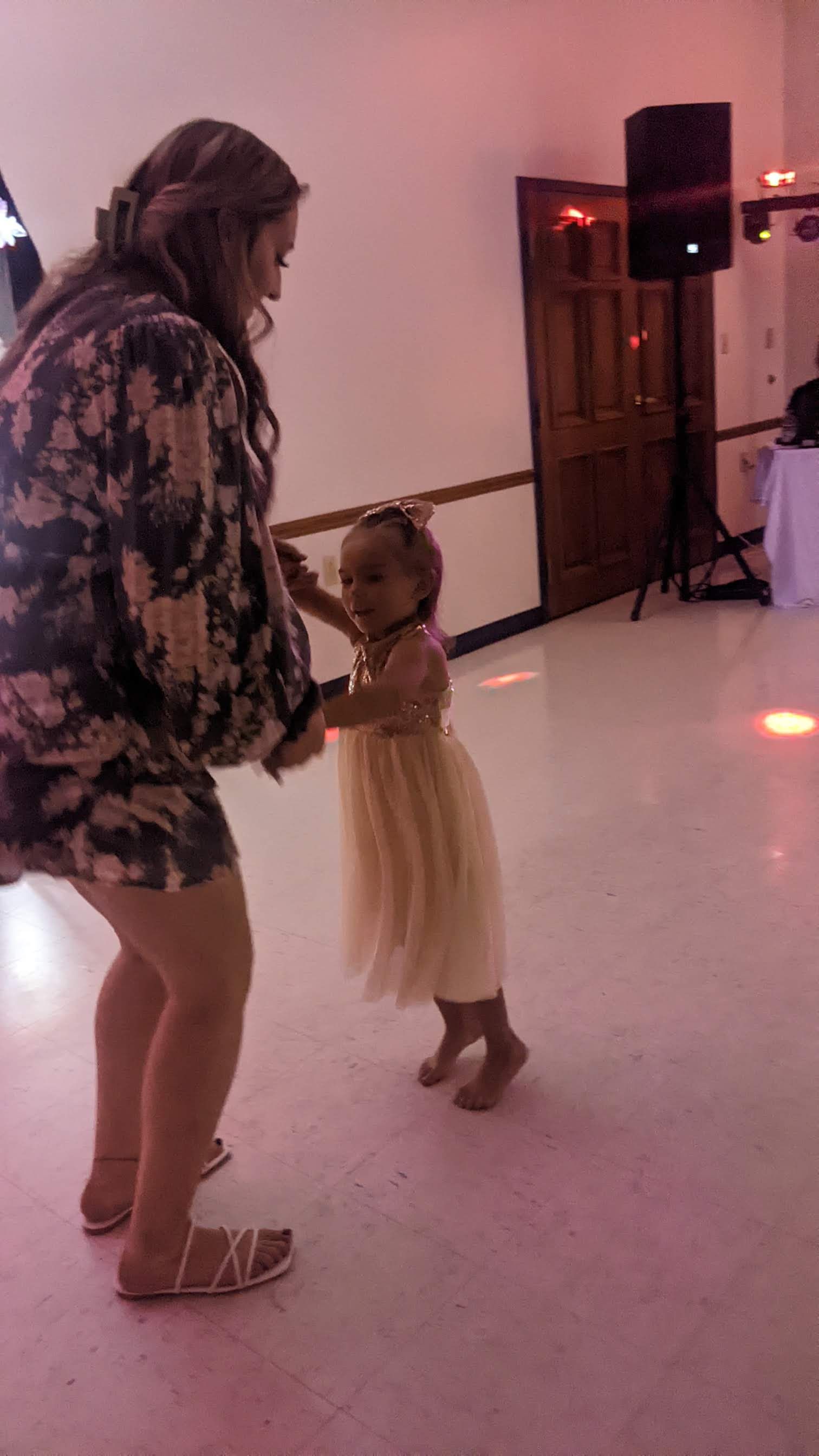 Two people dancing in a hall, holding hands under soft pink lighting.