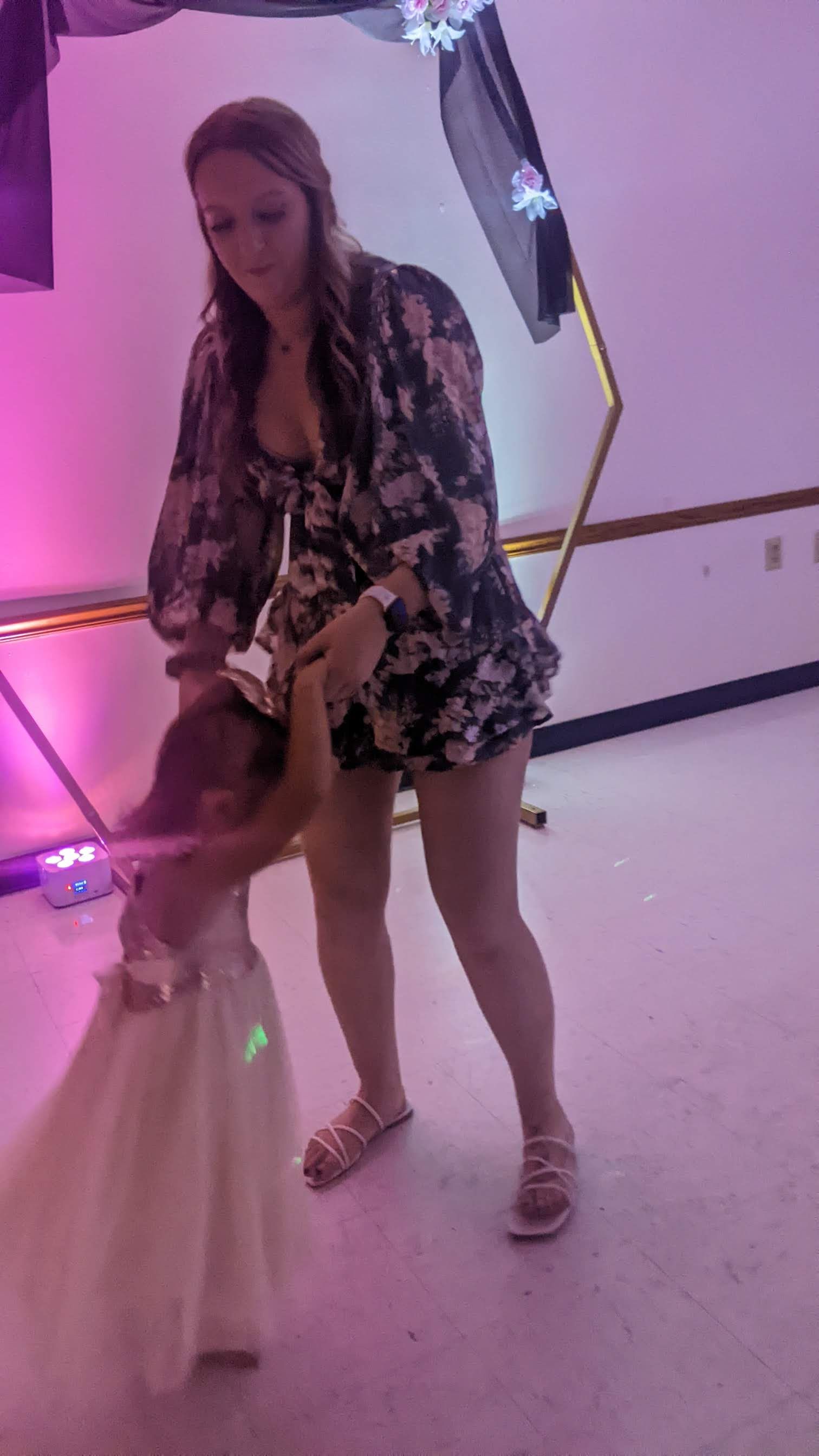 Woman in a floral dress holding a dog leash at a colorful indoor event.