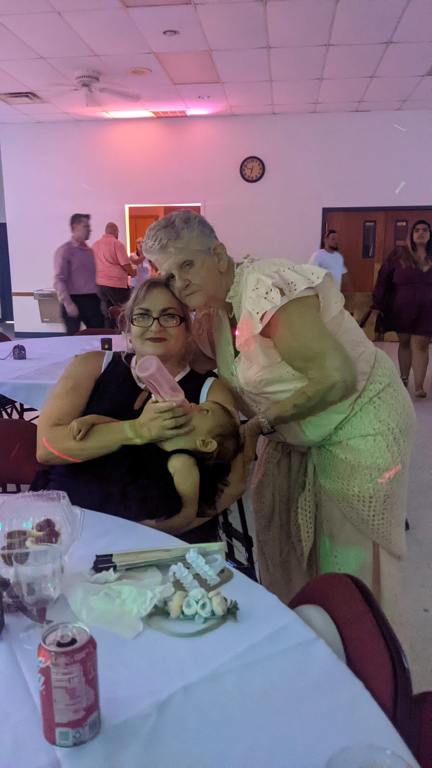 Person leaning over seated guest at a banquet table in a pink-lit event hall