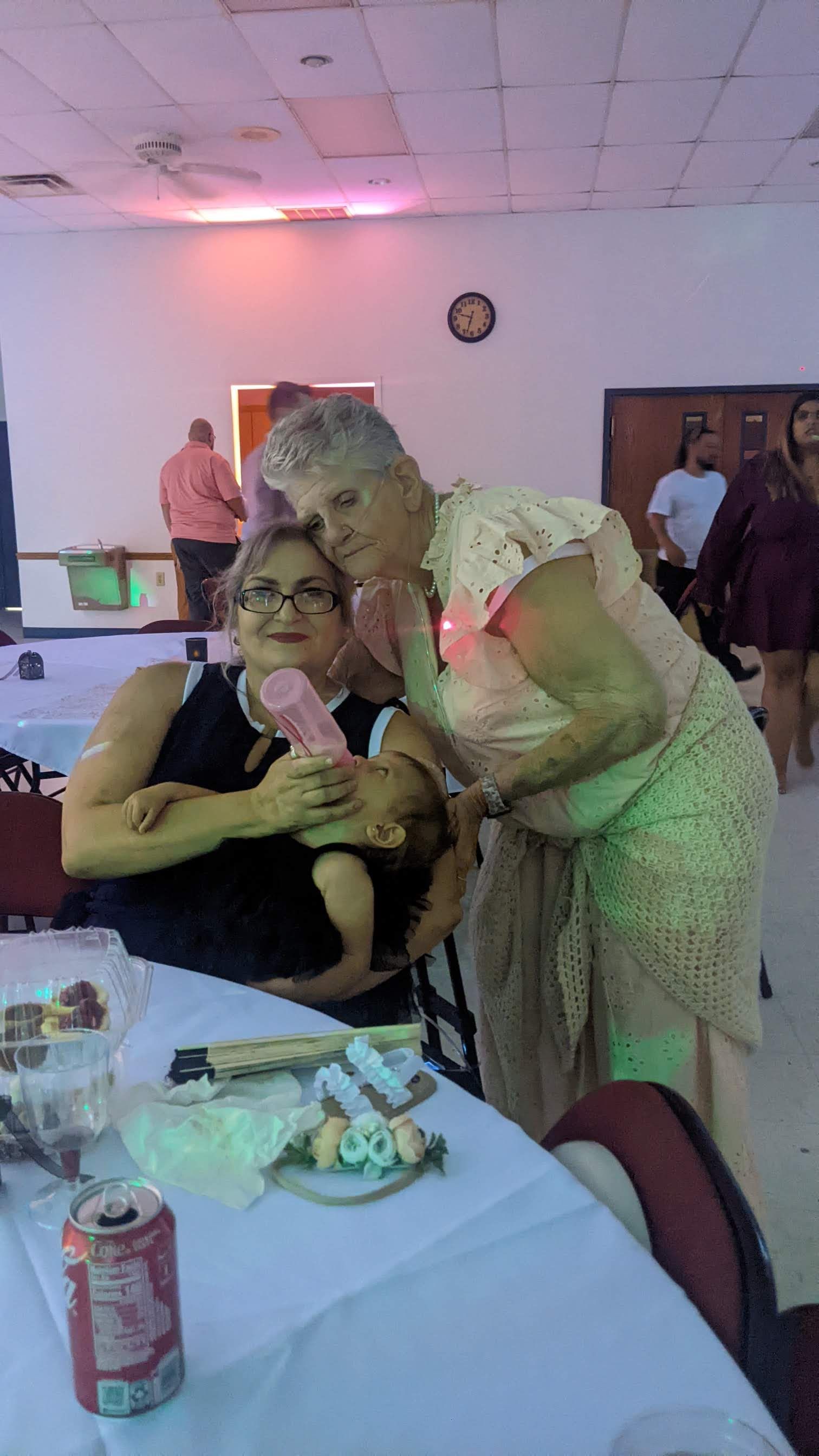 Woman in a green dress leans in to hug a seated woman holding a pink item at a banquet table.