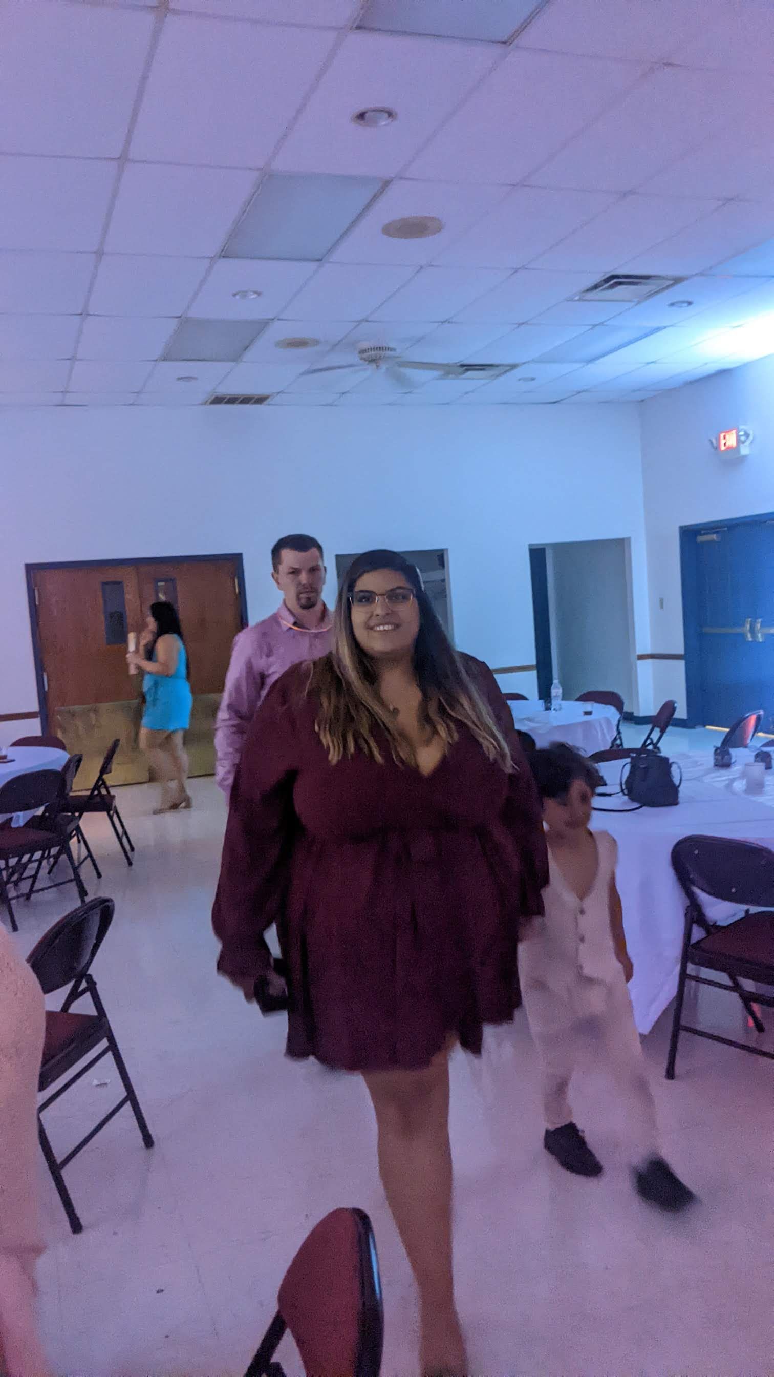 Two people walk through a banquet hall with chairs, under blue and purple lighting.