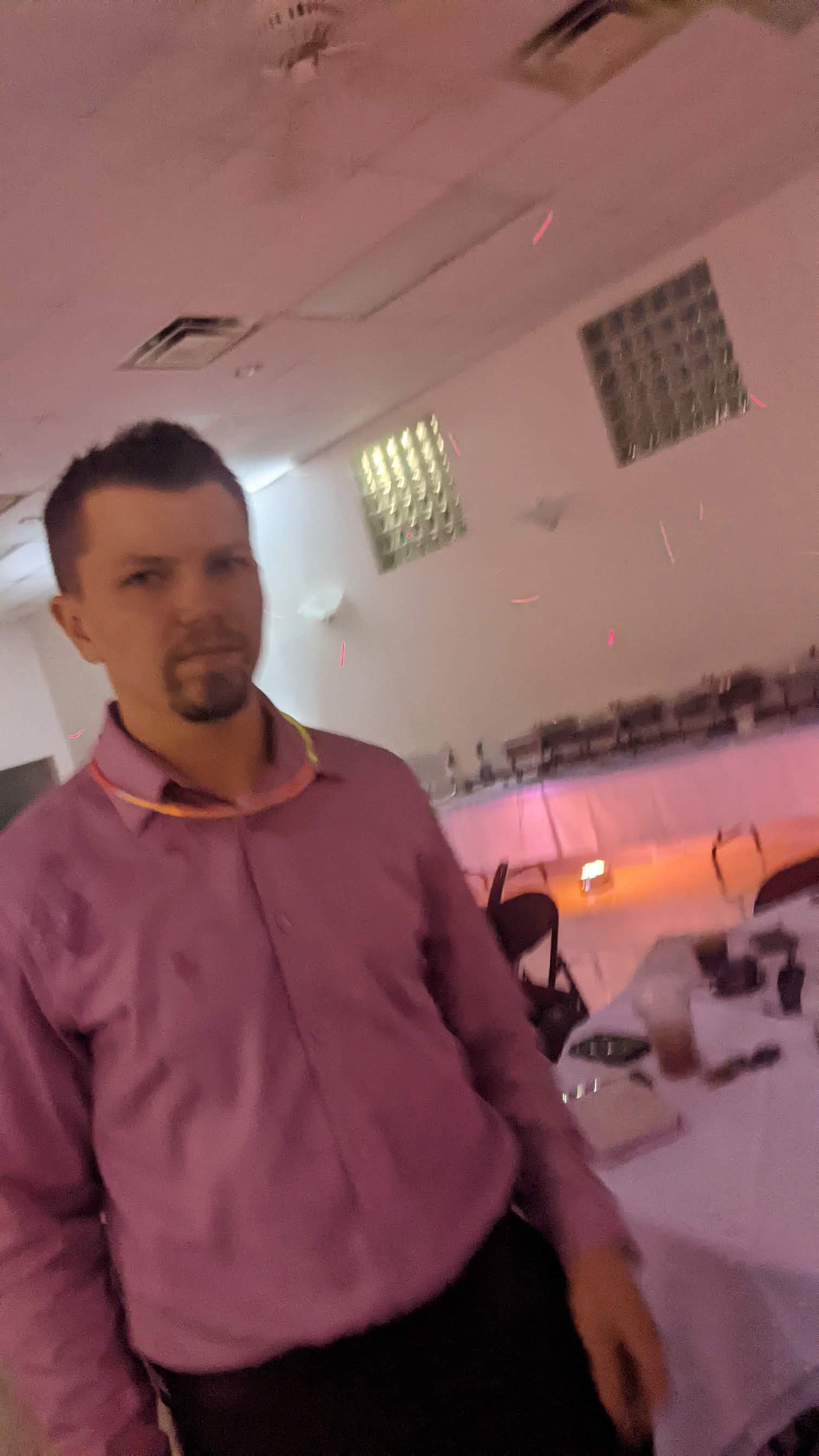 Man in a pink shirt standing at a banquet table in a softly lit event hall