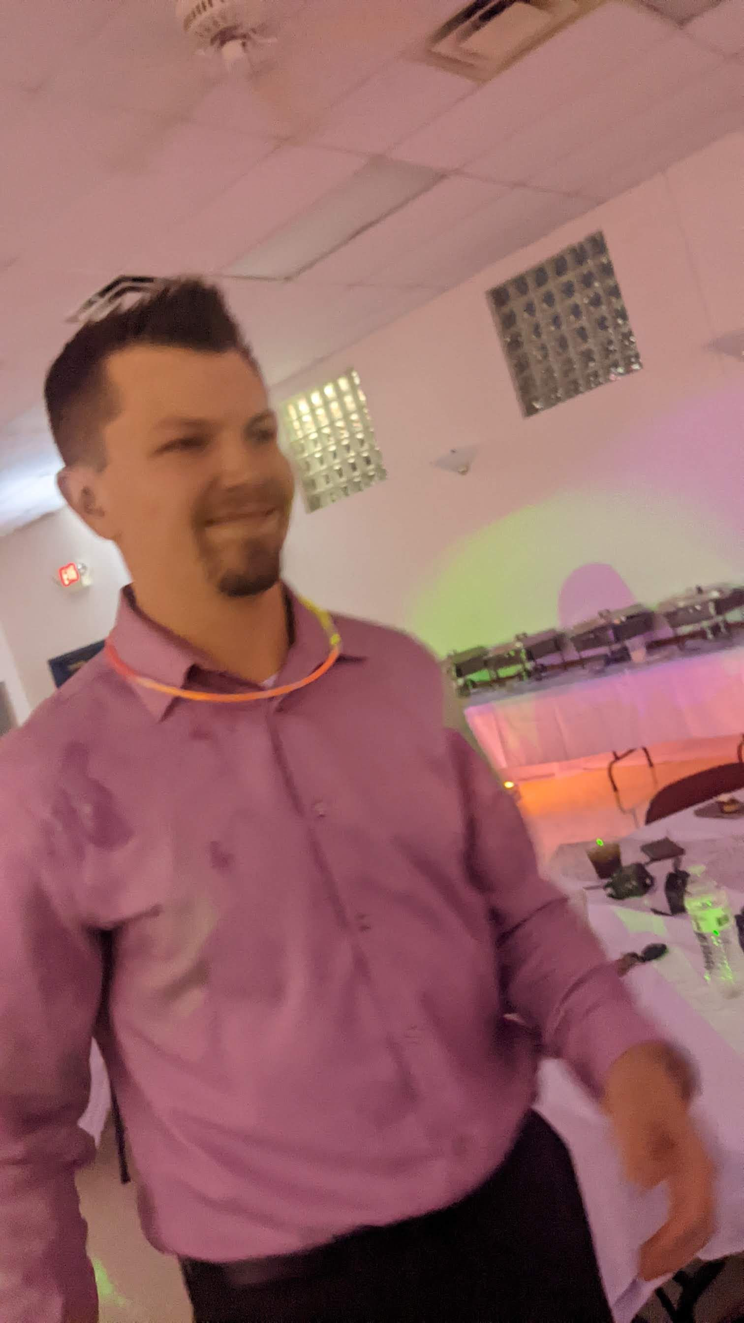 Man in a pink shirt standing in a softly lit indoor event space.