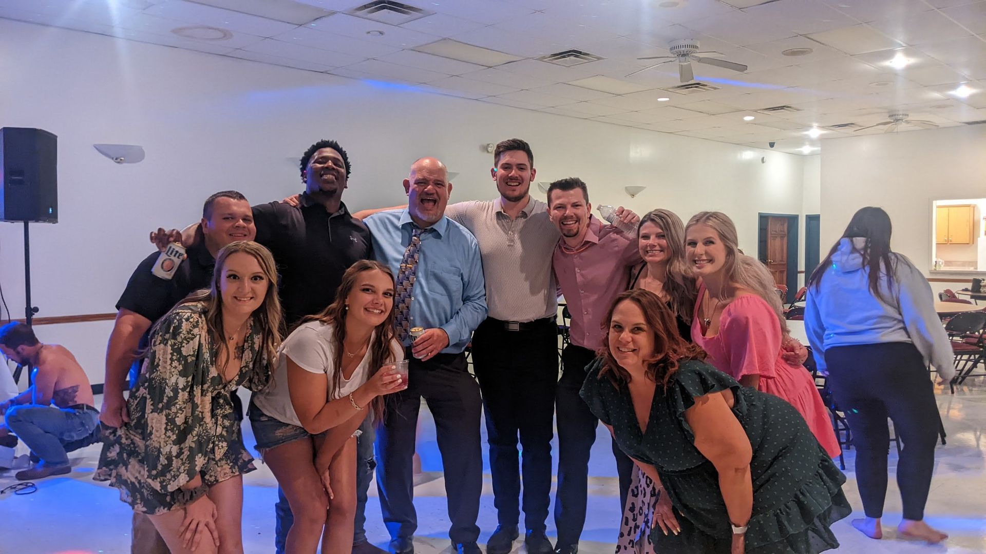 Group of people posing and smiling in a bright party hall with blue lighting