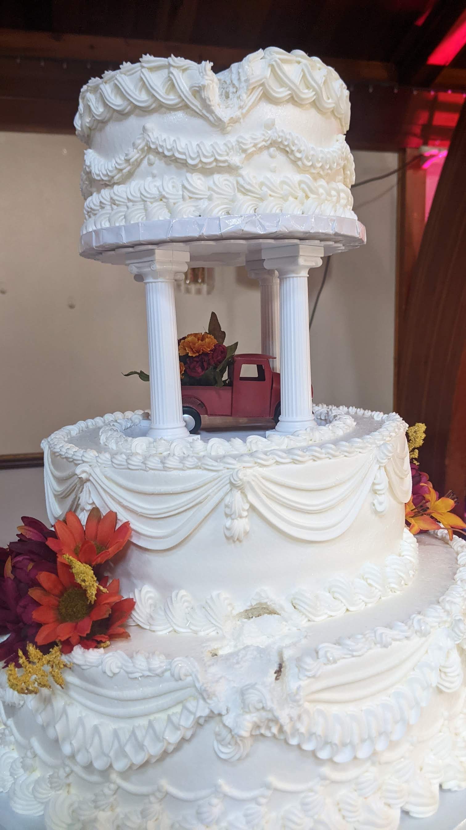White tiered wedding cake with ornate frosting, columns, and autumn leaves decoration