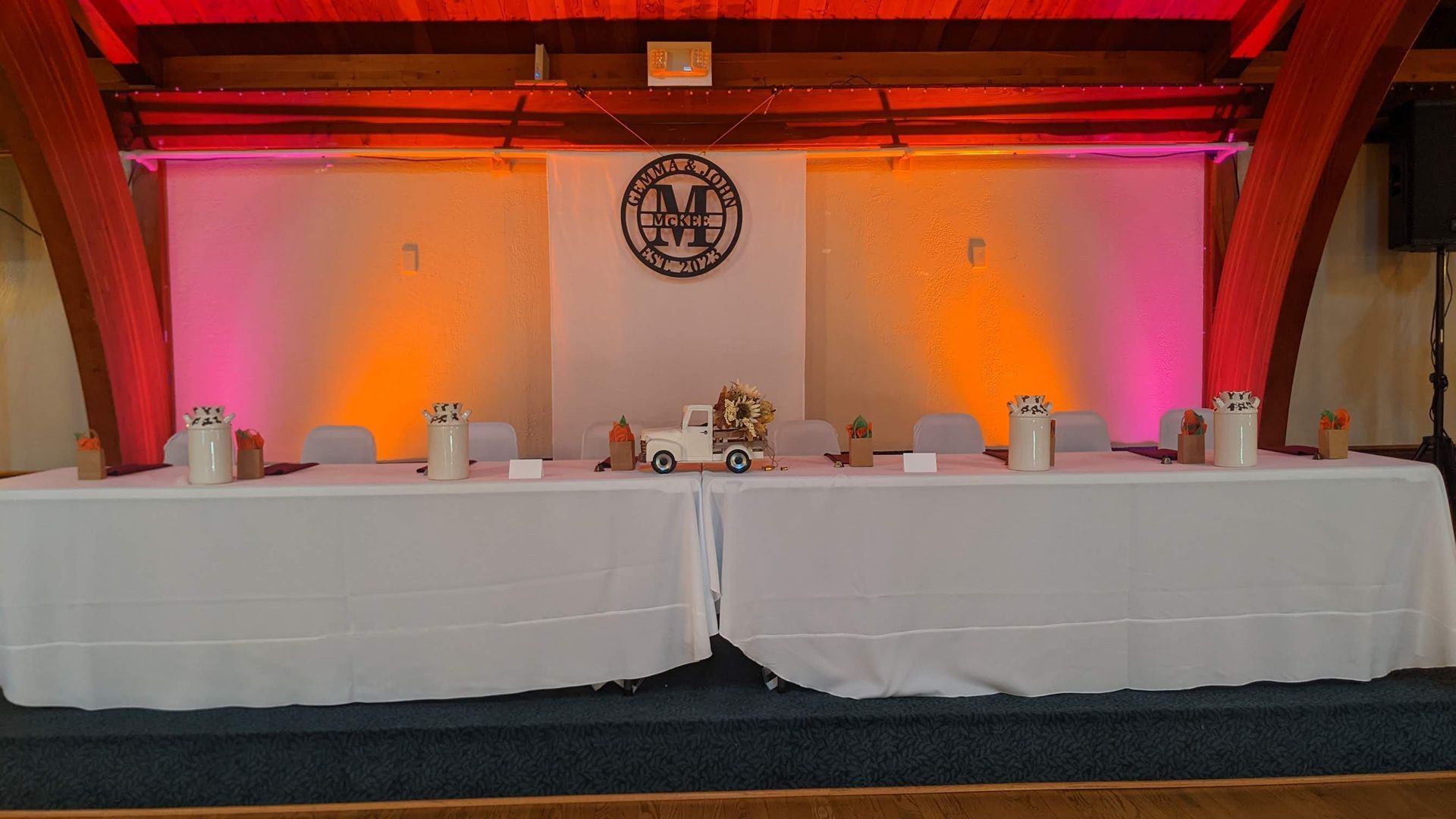 Banquet table with white cloths and centerpieces on a stage under warm red and orange lighting