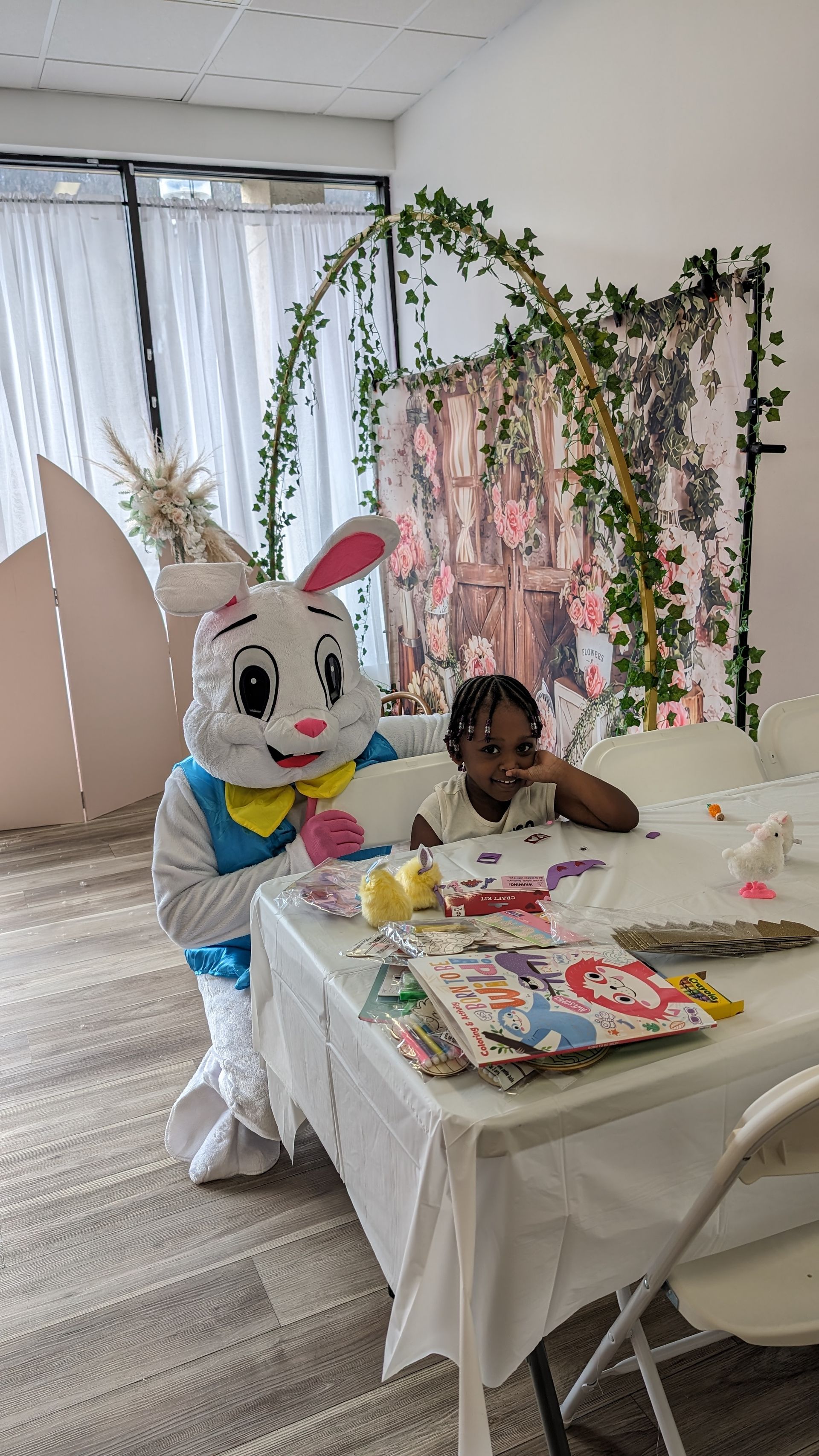 Child at a decorated table beside a white bunny mascot in a bright party room